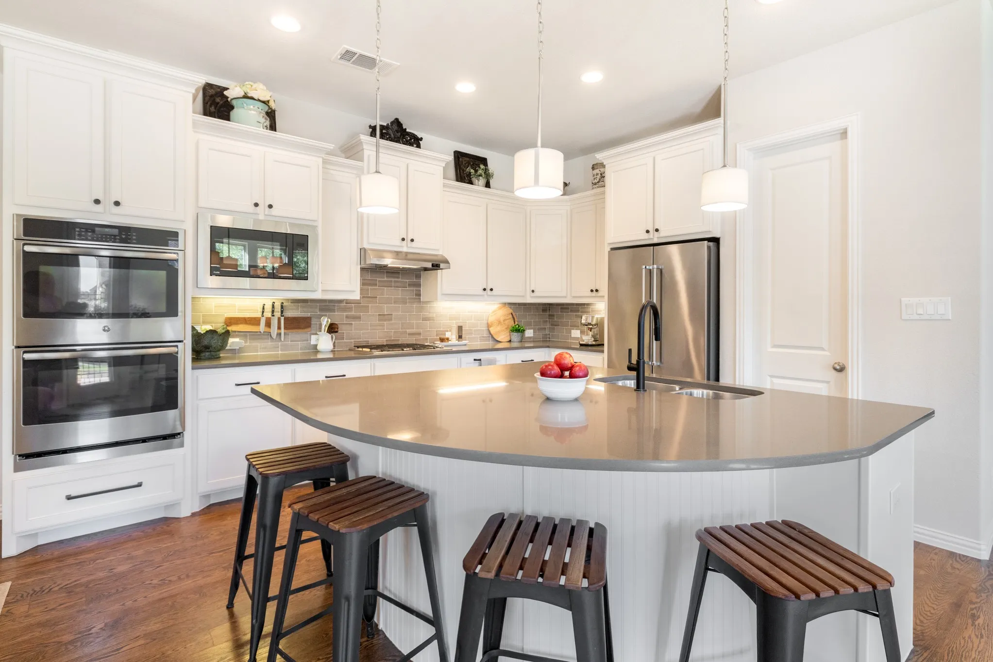 Curved kitchen island with integrated sink, stainless steel appliances, white cabinetry, and wood-finish flooring