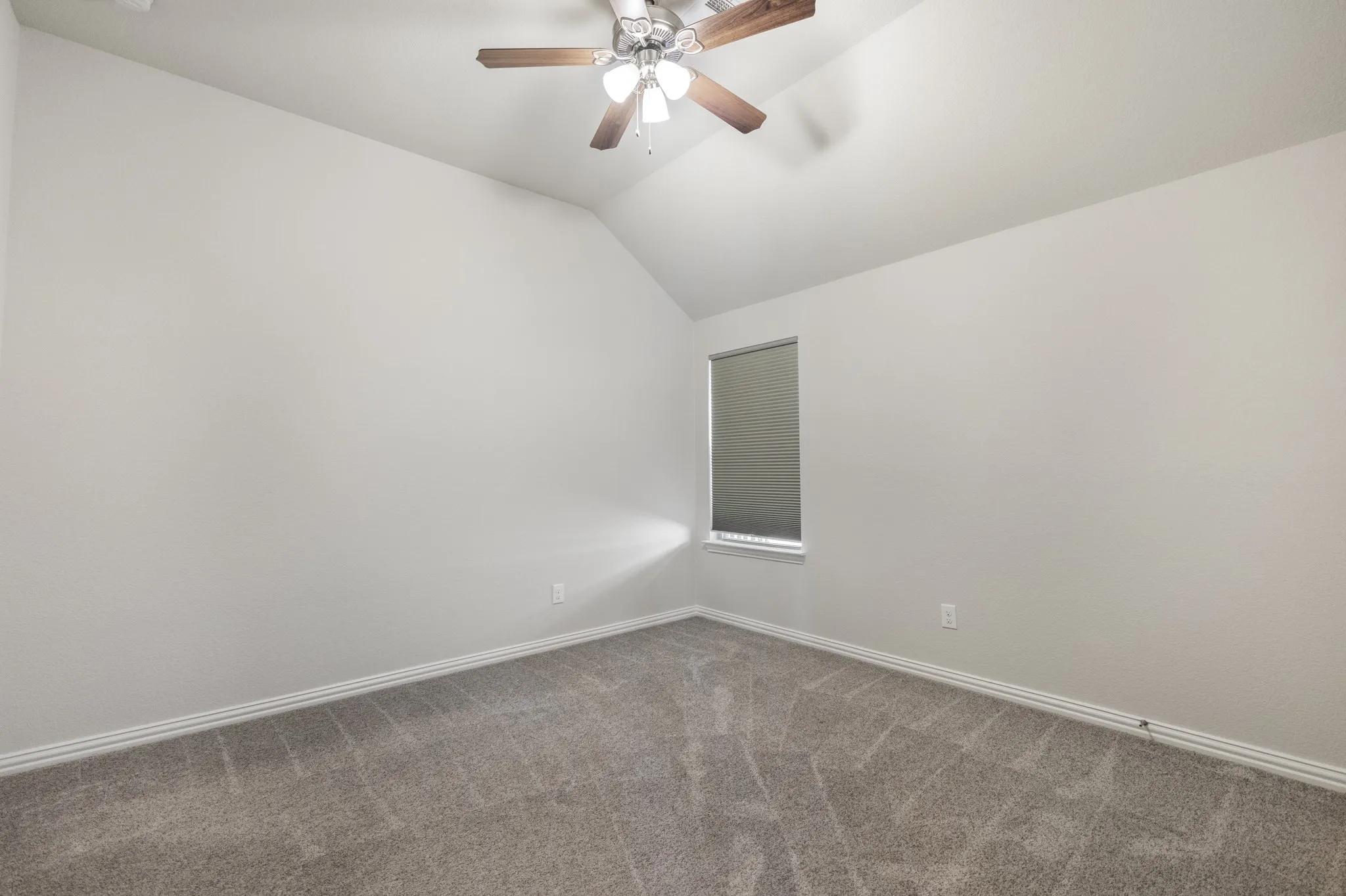 Upstairs, third bedroom with vaulted ceiling featuring a ceiling fan, neutral wall paint, gray carpet, and a window with a roller shade