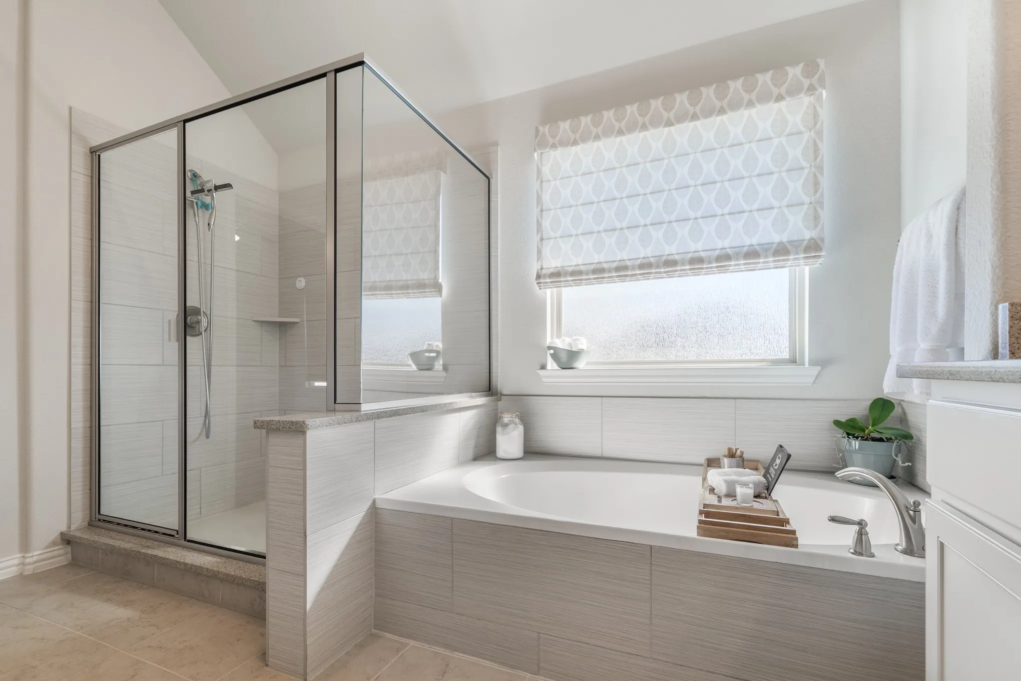 Built-in soaking tub with deck-mounted faucet, tile surround, and adjacent glass-enclosed shower with tiled walls and built-in shelf