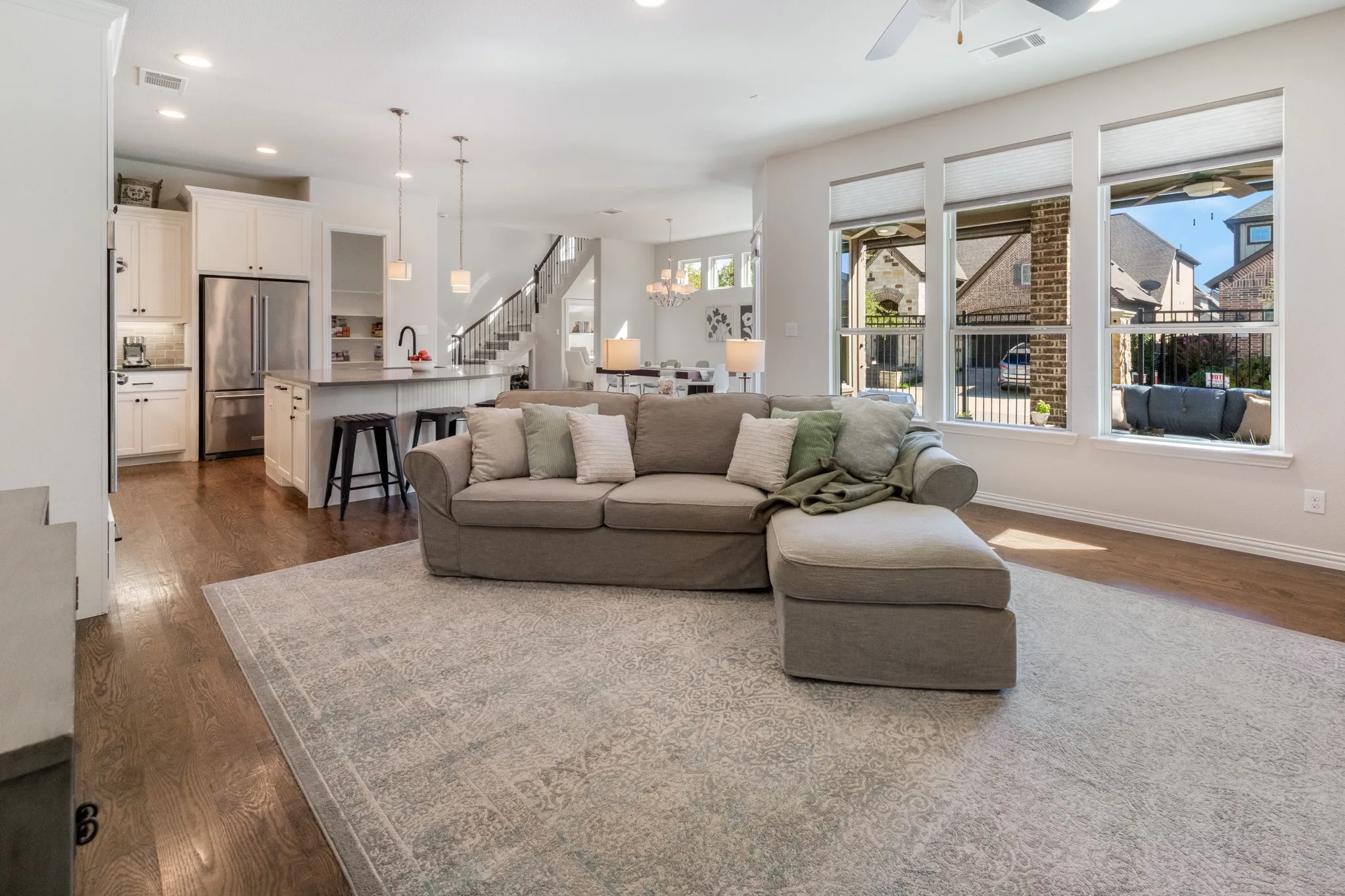 Open-concept living area featuring wood-finish flooring, a kitchen island with seating, white cabinetry, stainless steel appliances, and a wall of windows