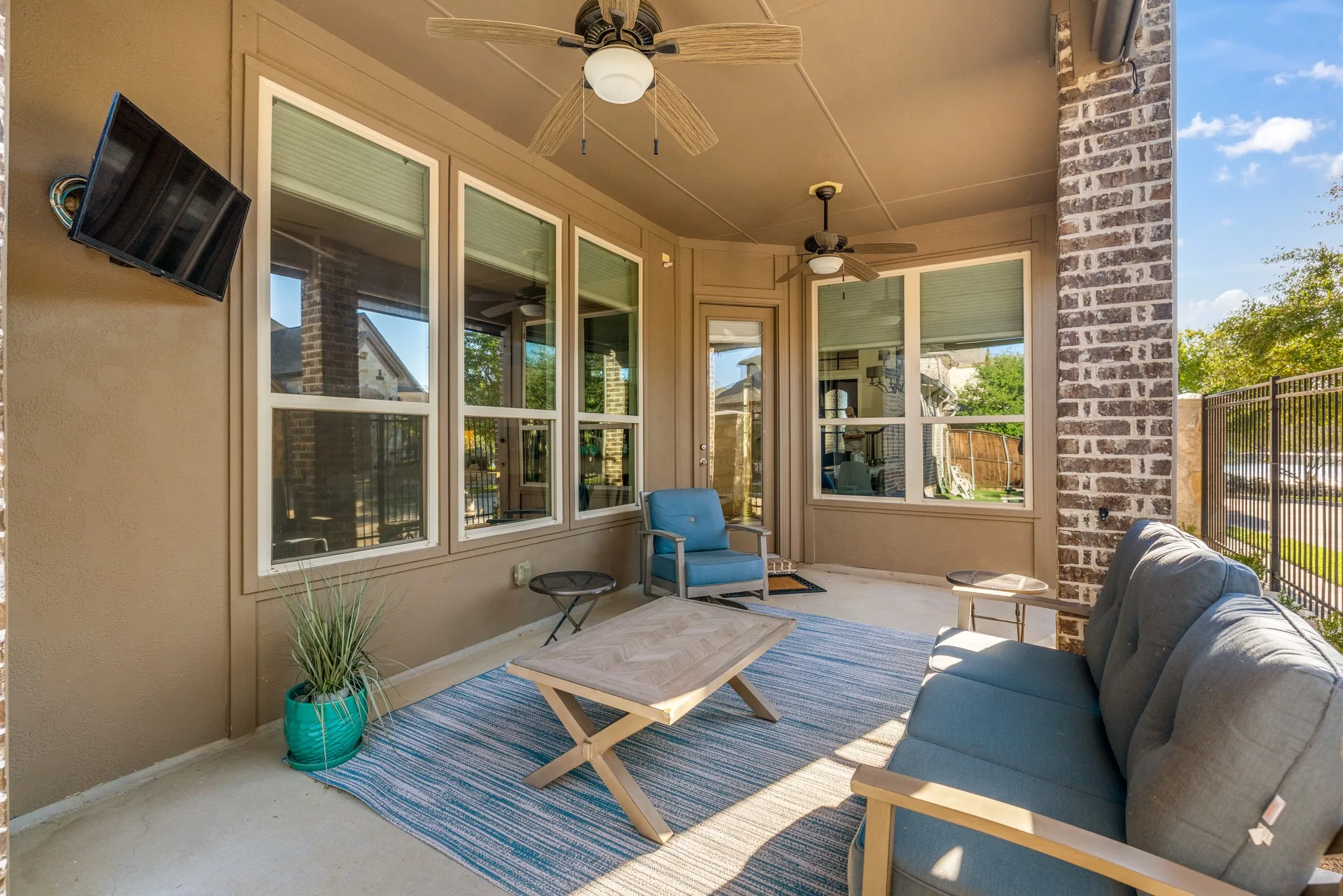 Covered patio featuring a concrete slab, brick support columns, multiple windows, and two ceiling fans