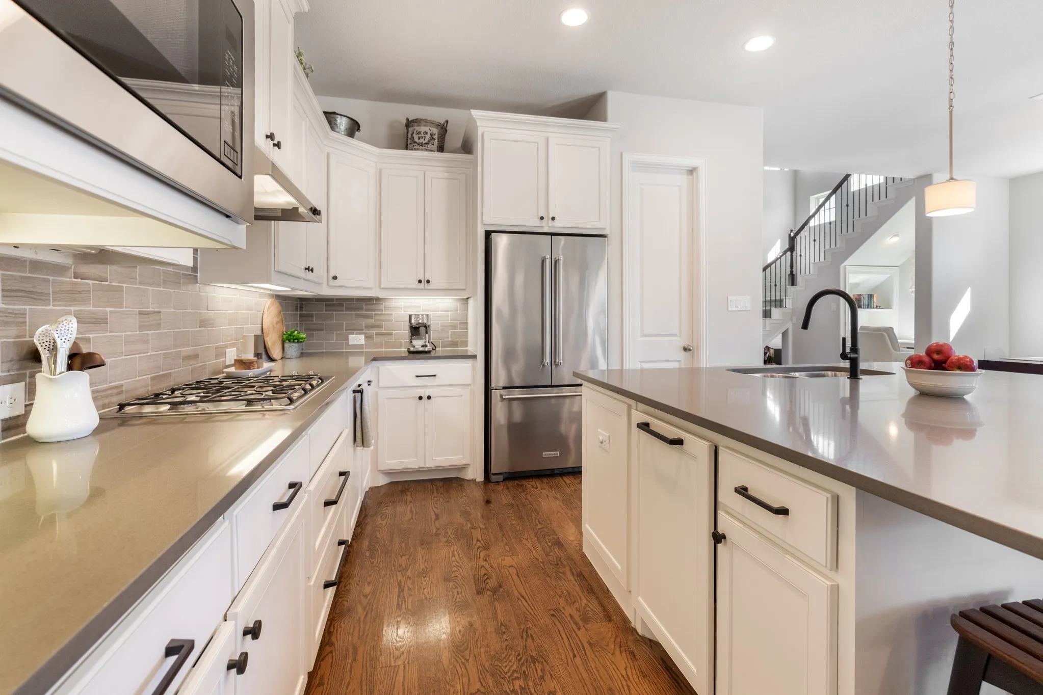 White shaker cabinetry with dark hardware, stainless steel appliances, light-toned countertop surfaces, a subway tile backsplash, and dark wood-finish flooring