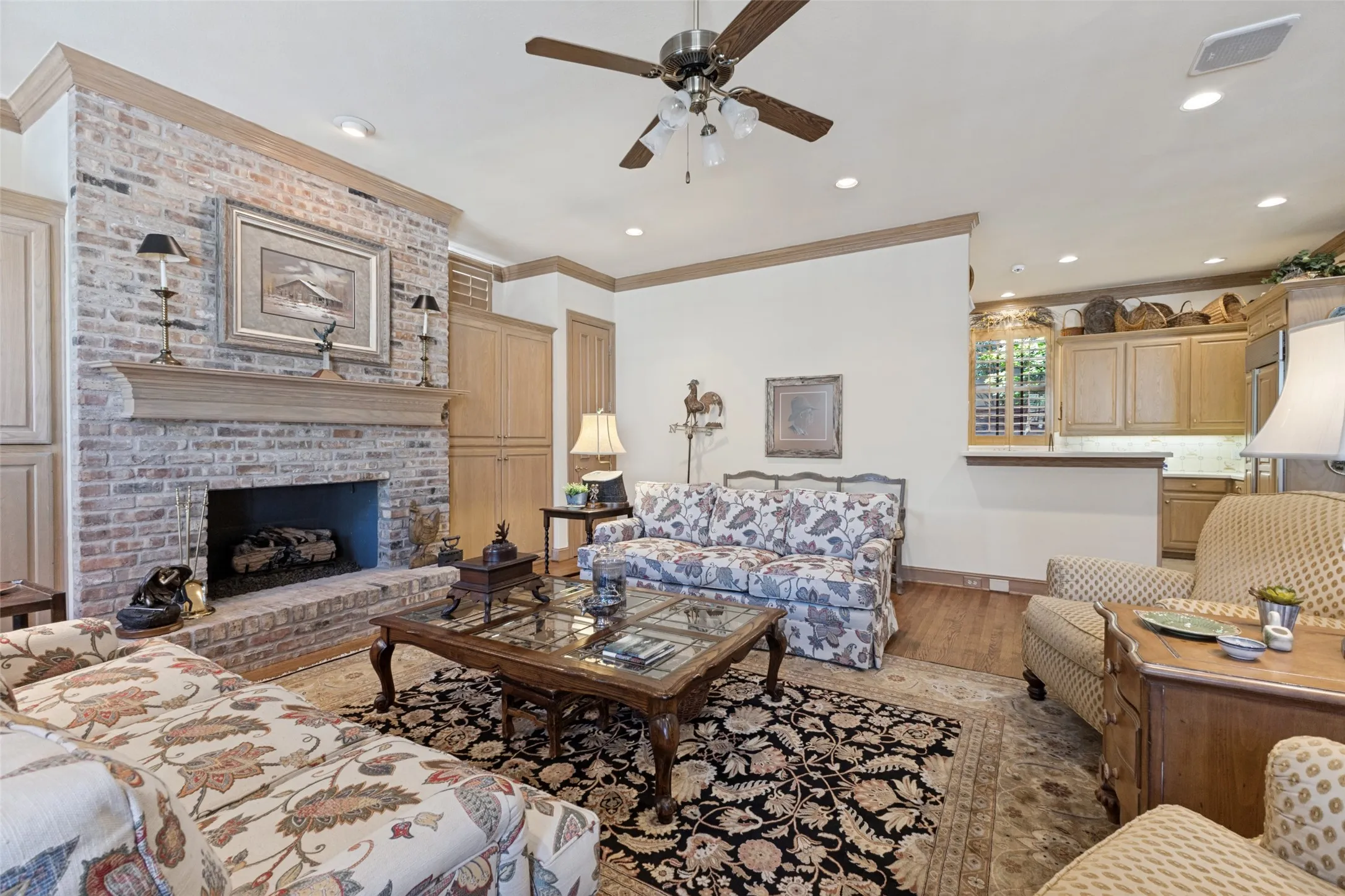 Brick fireplace with a wood mantle, built-in cabinetry, wood-finish flooring, and recessed lighting