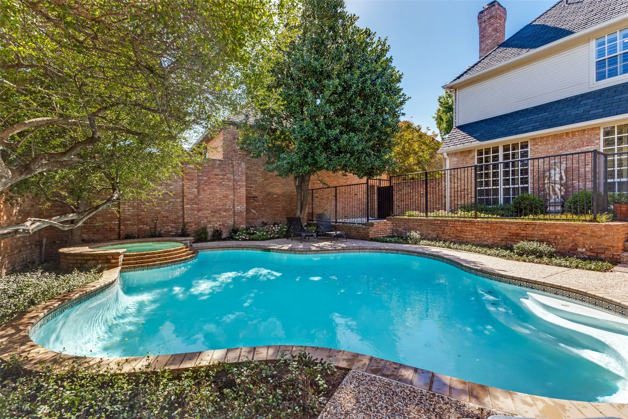 Freeform swimming pool with integrated spa and broad steps, surrounded by brick-edged coping and mature landscaping