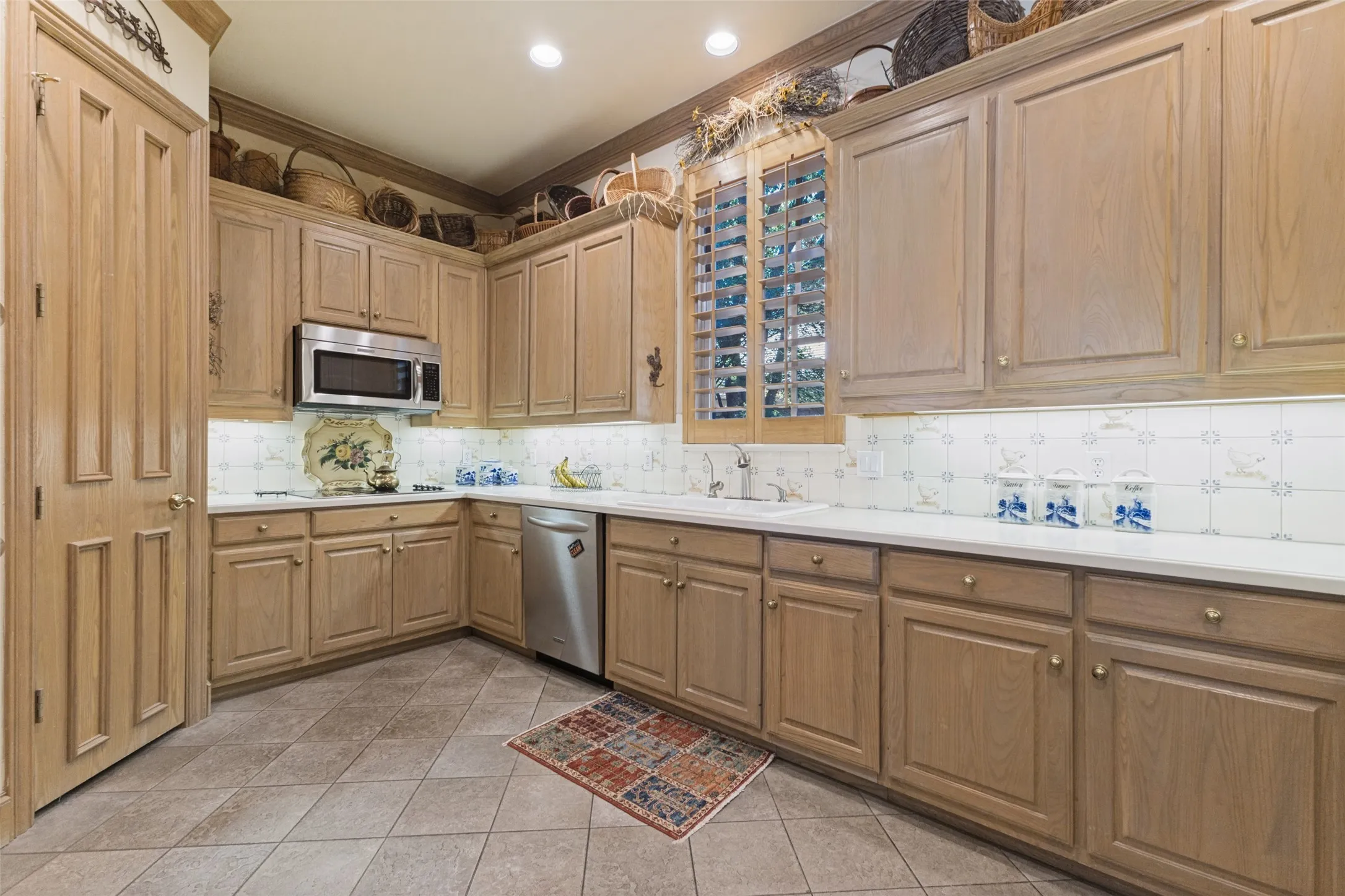 Kitchen featuring wood-finish cabinetry, stainless steel microwave, stainless steel dishwasher, white countertops, and tiled flooring
