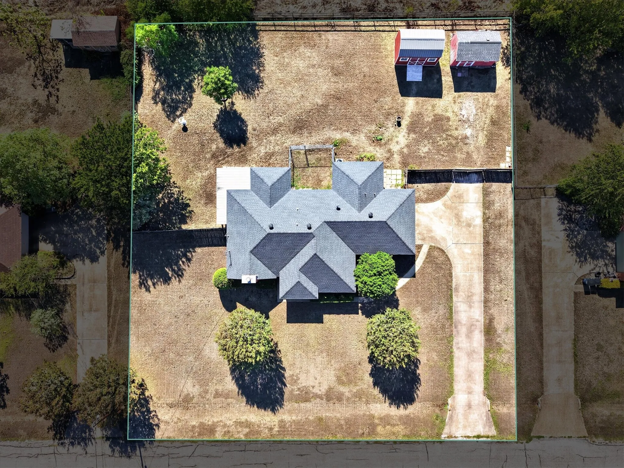 Expansive lot featuring a main residence with a multi-gabled roof, a concrete driveway, and two detached outbuildings