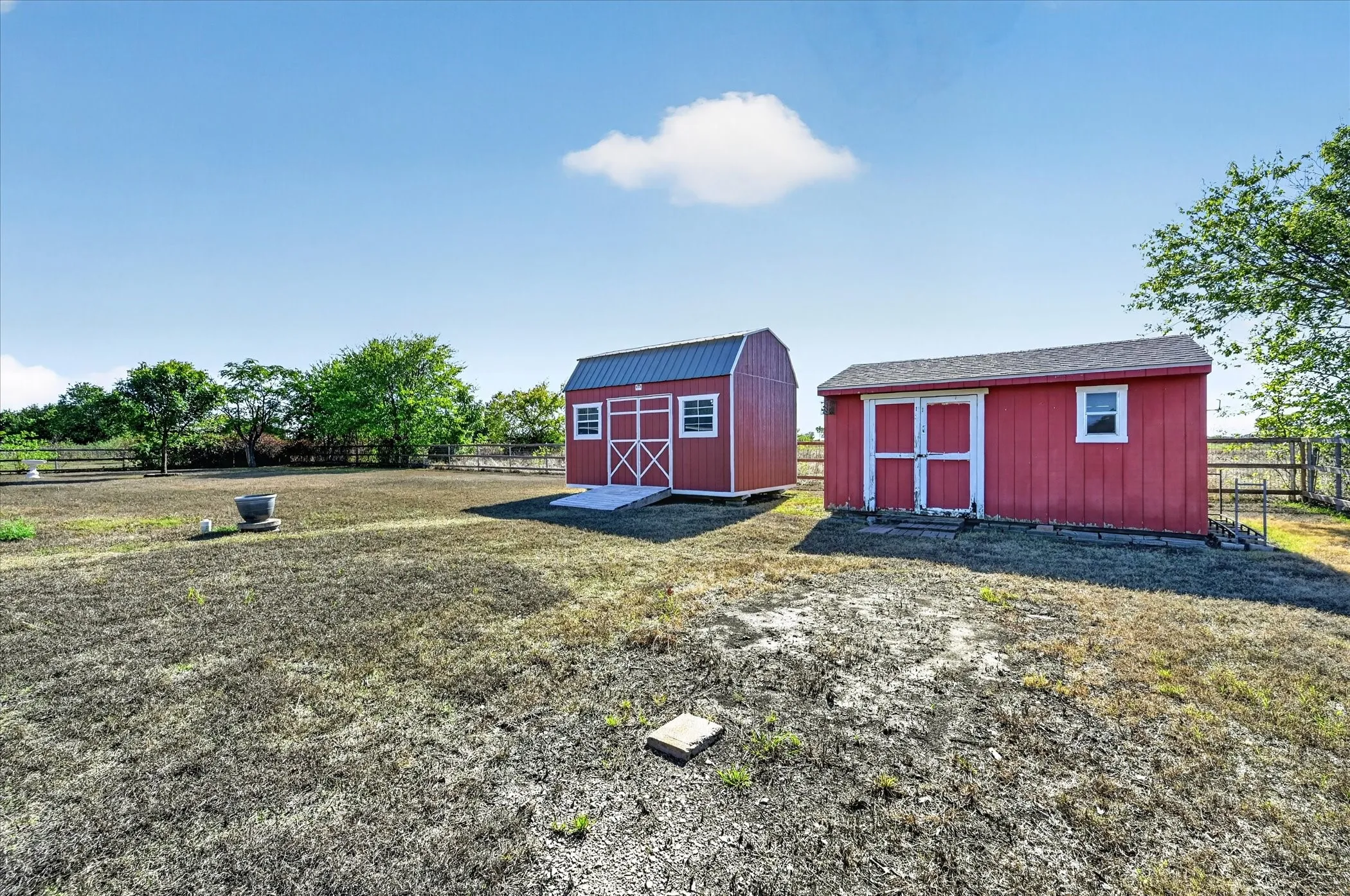 Two red storage sheds with white trim, one featuring a gambrel roof and the other a gabled roof