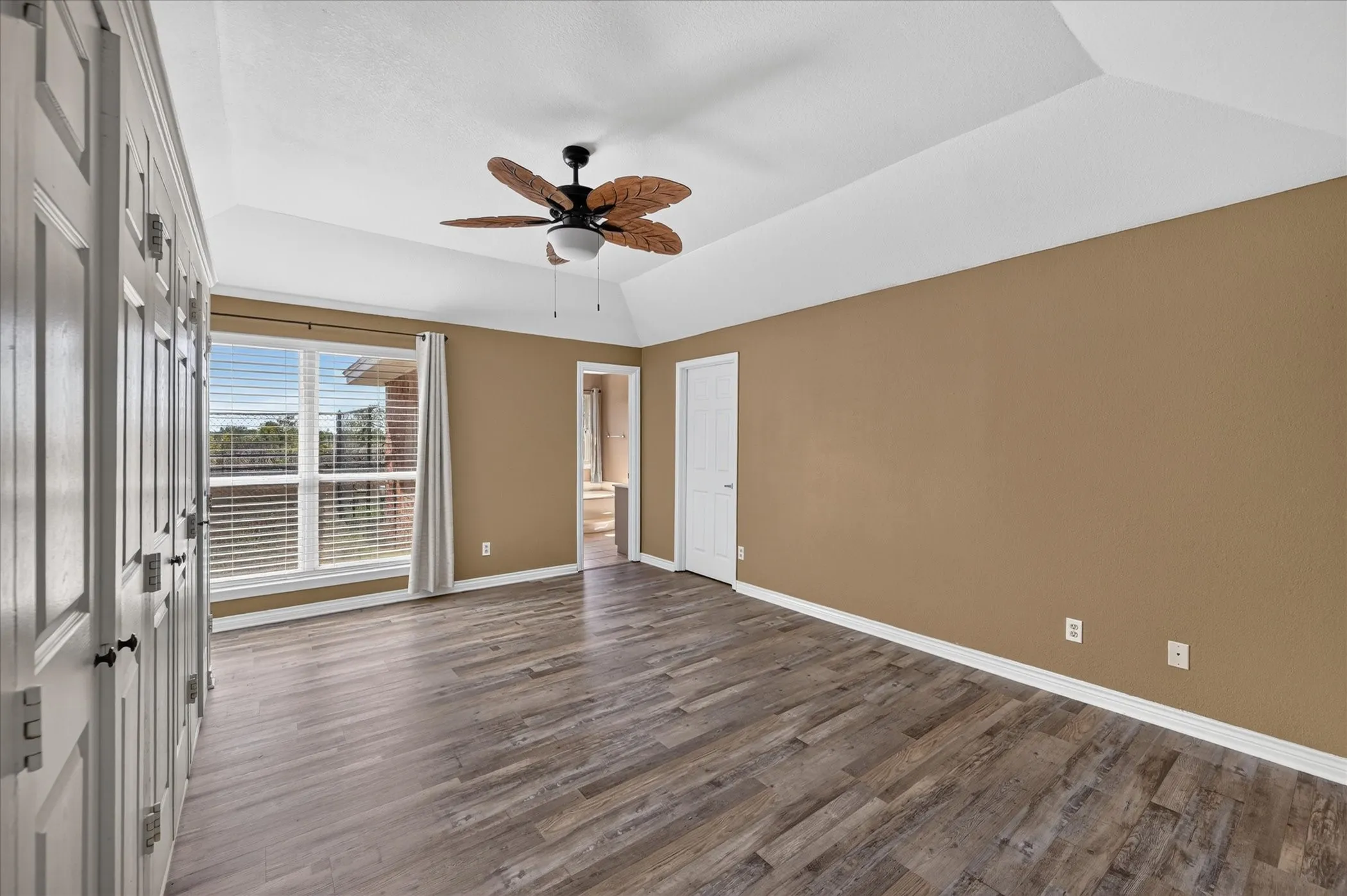 Vaulted ceiling, wood-finish flooring, ceiling fan, and large windows with blinds