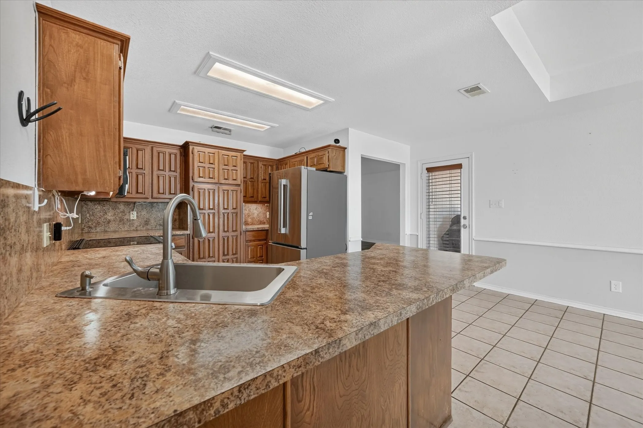 Kitchen featuring wood-finish cabinetry, stainless steel sink with a high-arc faucet, and a large breakfast bar