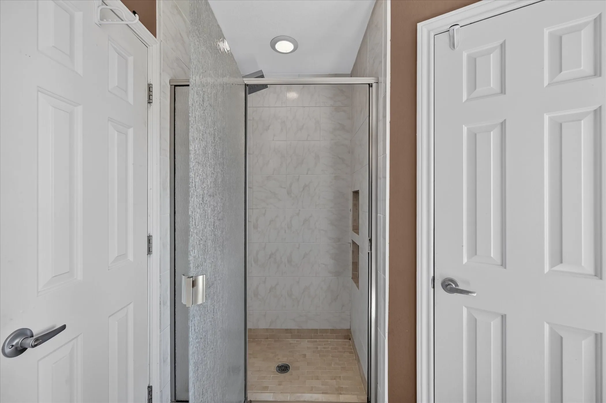 Enclosed shower with clear glass door, built-in shelving, tiled walls, and recessed lighting