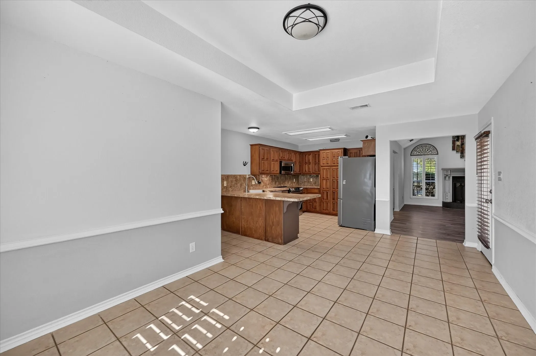 Tiled flooring throughout, kitchen featuring wood cabinetry and an integrated microwave, and an arched doorway leading to an additional space with a large arched window