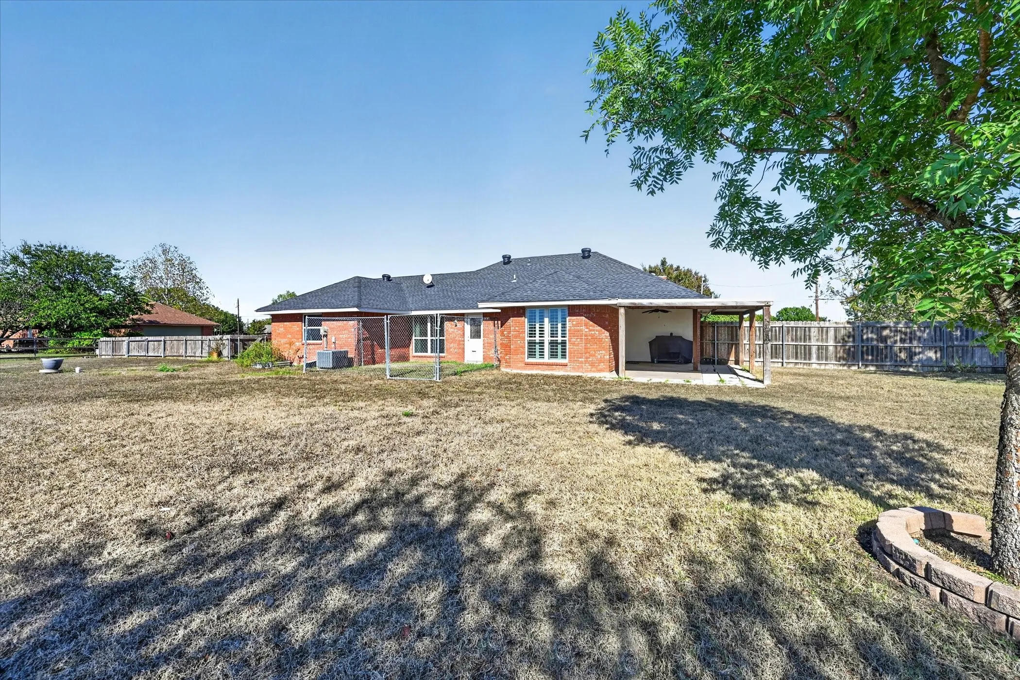 Expansive backyard featuring a red brick exterior, covered patio, and mature trees