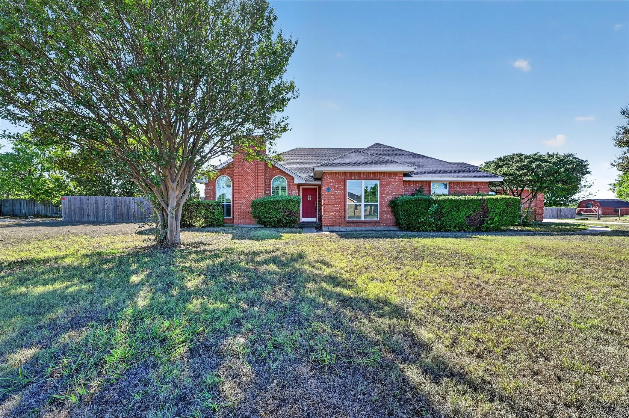 Red brick exterior with arched windows, a dark shingle roof, and established landscaping