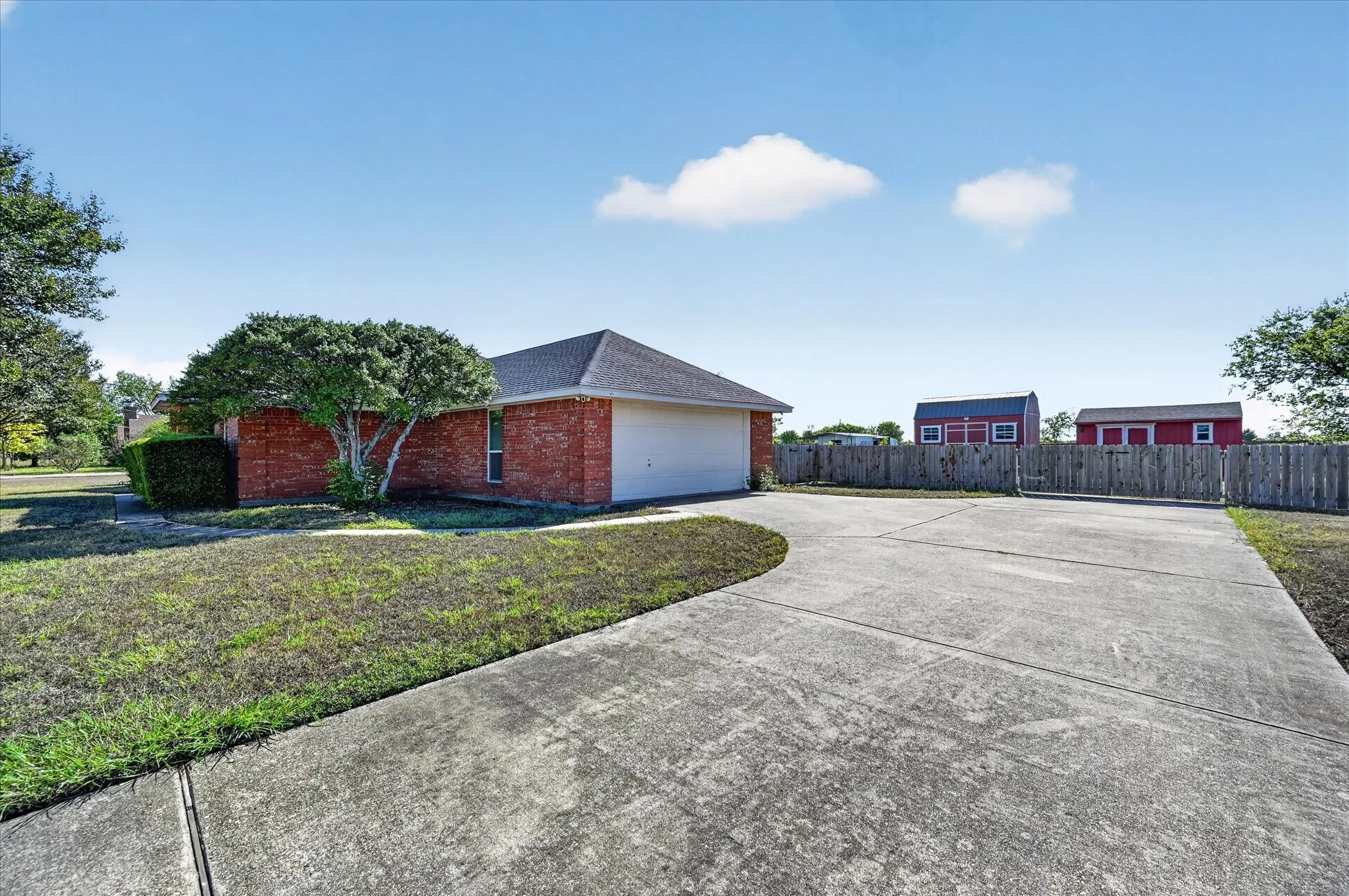 Brick exterior, attached two-car garage, concrete driveway, wood privacy fence, and two red storage sheds