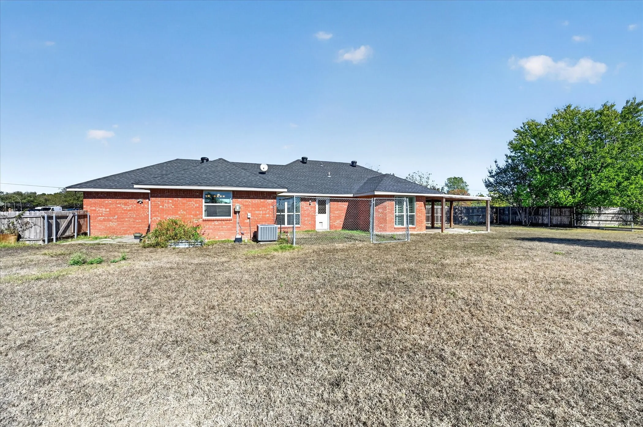 Expansive yard with a brick exterior, covered patio, and a dark shingle roof
