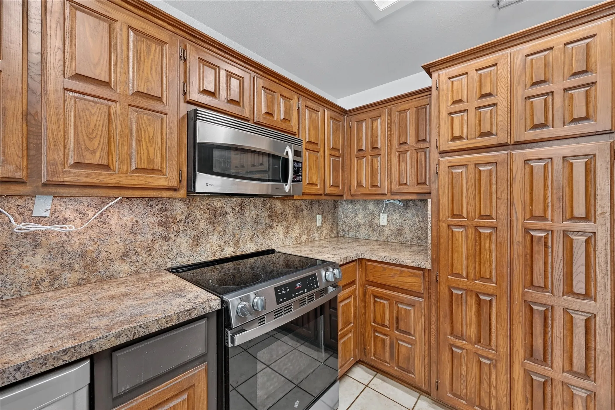 Extensive wood-finish cabinetry, stainless steel microwave, and cooktop with integrated oven