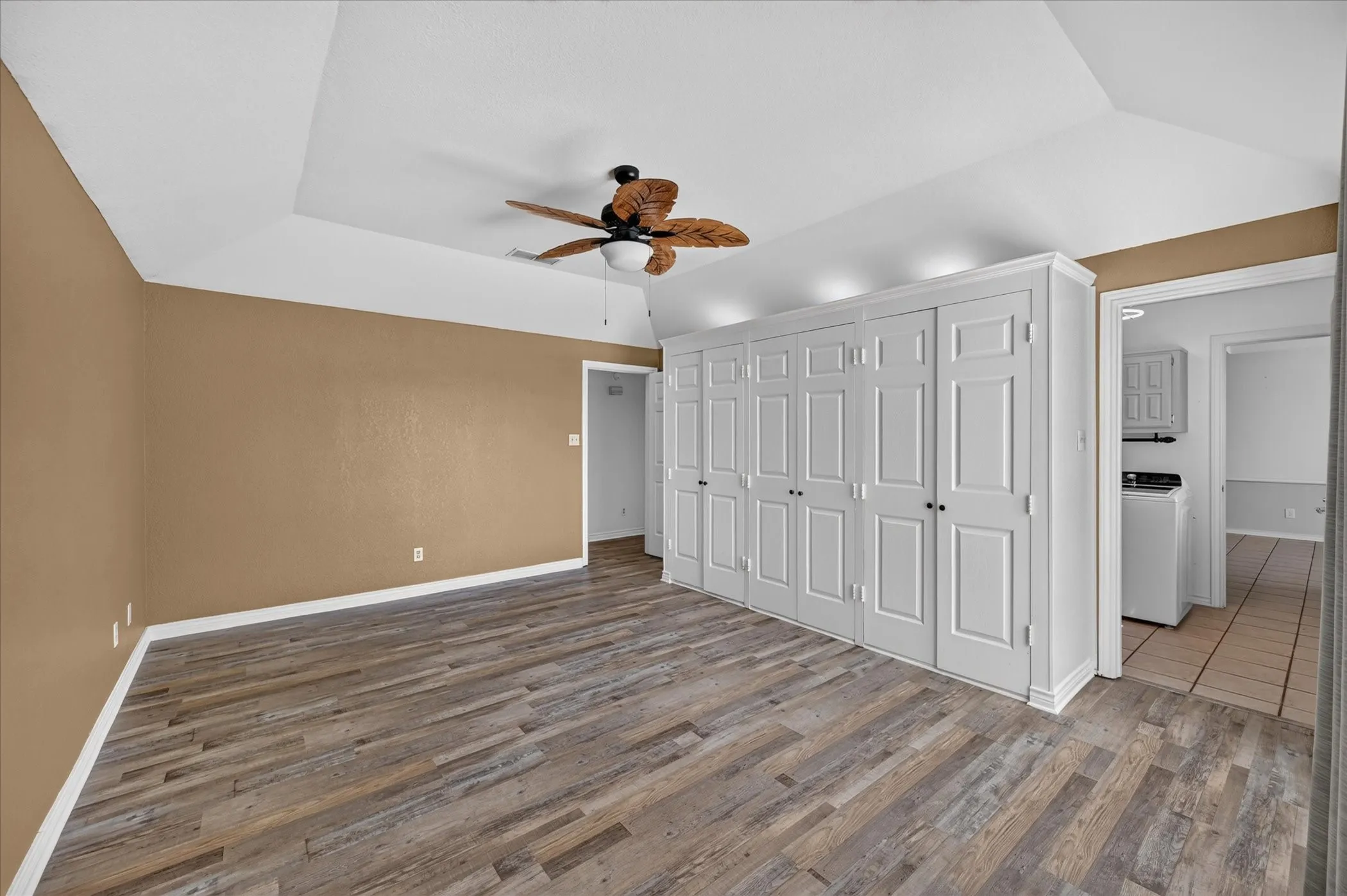 Vaulted ceiling, ceiling fan with light, wood-finish flooring, built-in storage cabinetry, and white trim