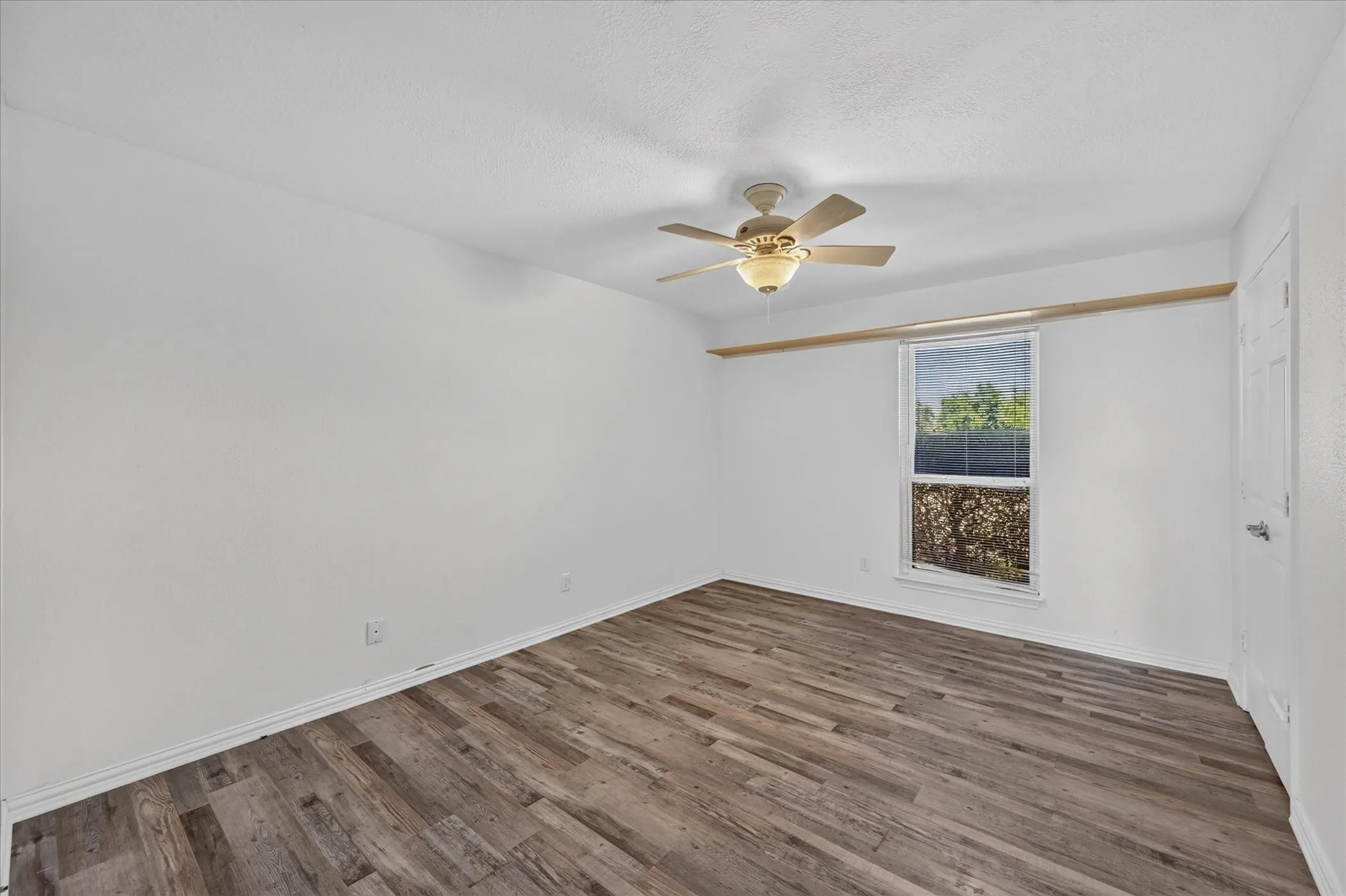 Ceiling fan with integrated lighting, wood-finish flooring, white painted walls, and a window with blinds