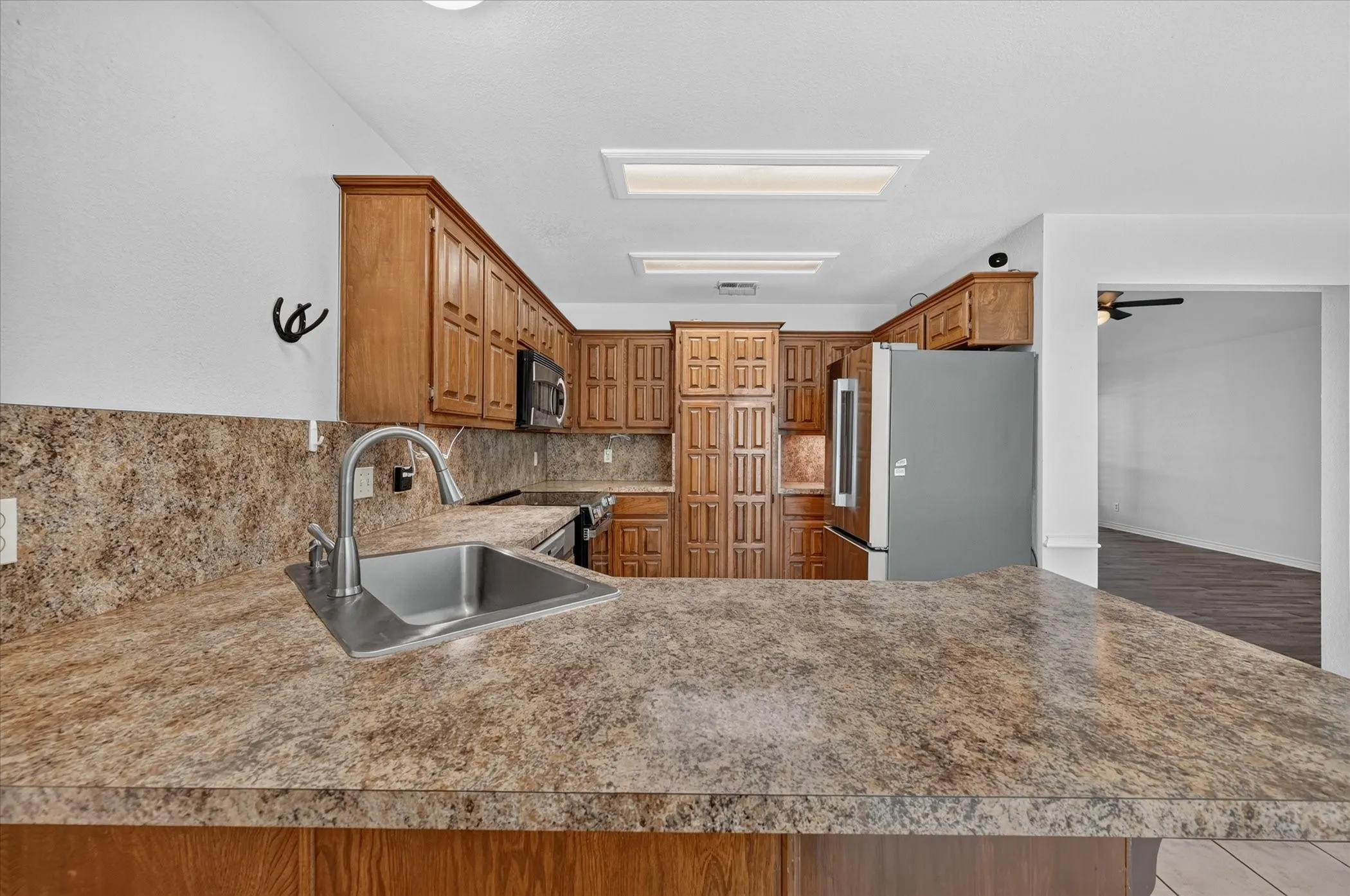 Kitchen featuring wood cabinetry, stainless steel sink with a high-arch faucet, and patterned countertops