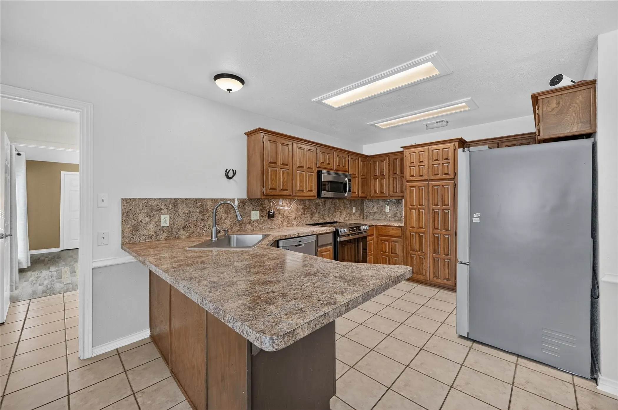Kitchen featuring wood cabinetry, laminate countertops, tile flooring, and stainless steel appliances