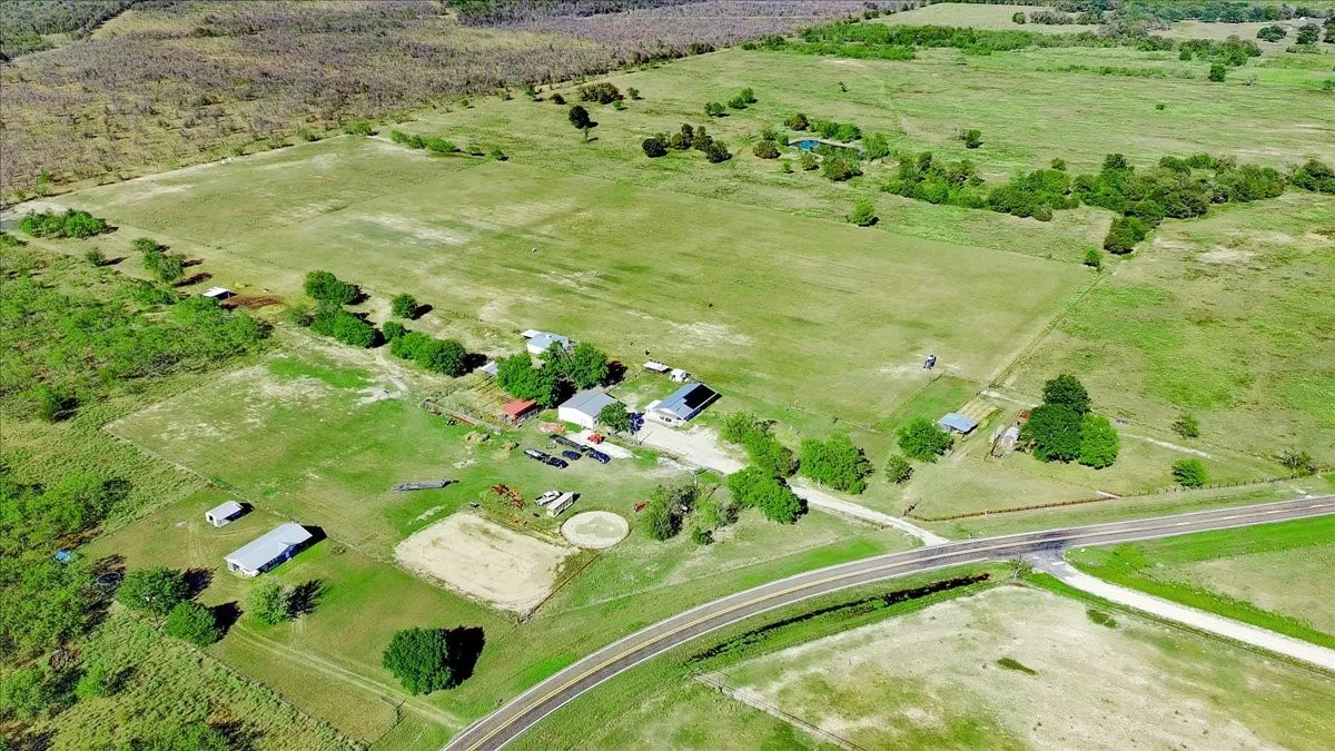 Expansive agricultural property featuring multiple structures, open fields, and access to a paved road