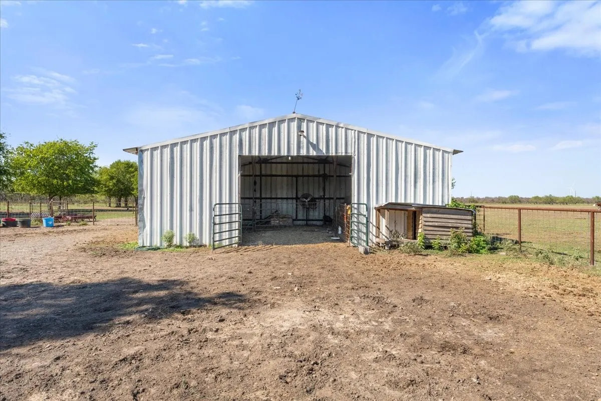 Metal-sided barn structure with an open entrance and partial fencing