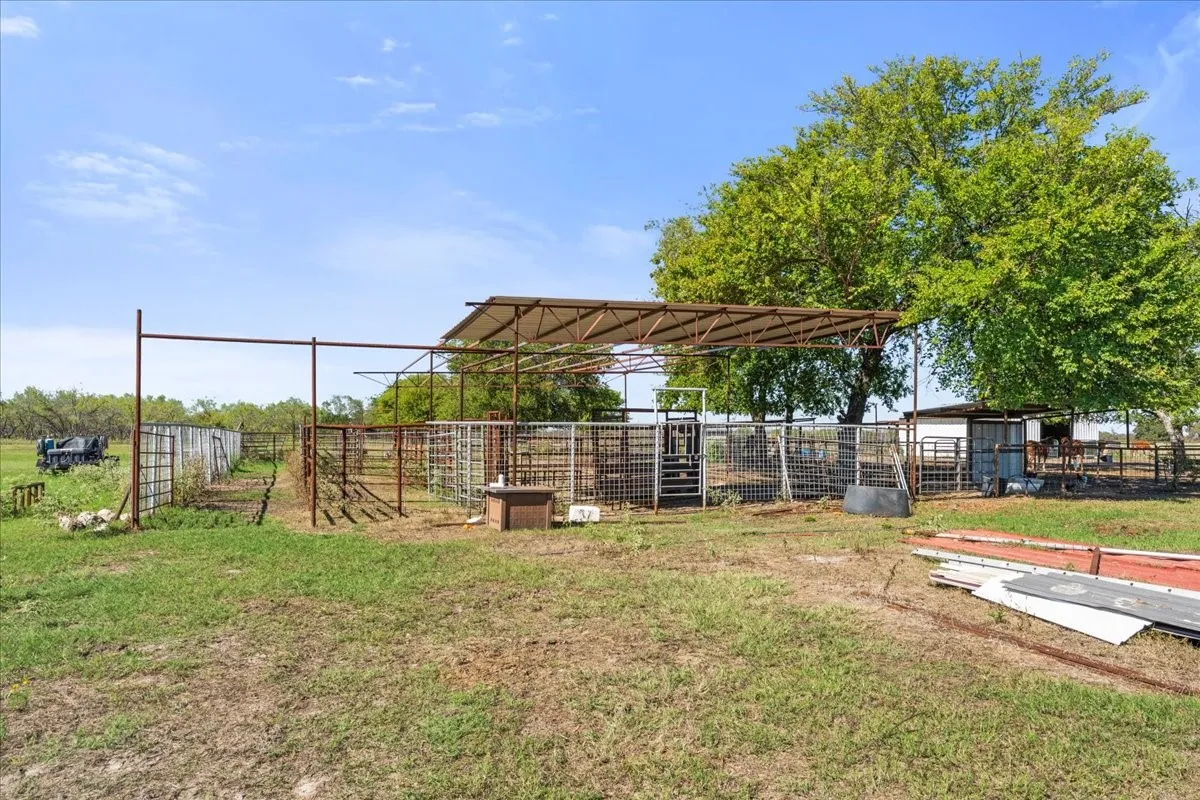 Expansive fenced paddock with a partial shade structure, multiple pens, and a large mature tree