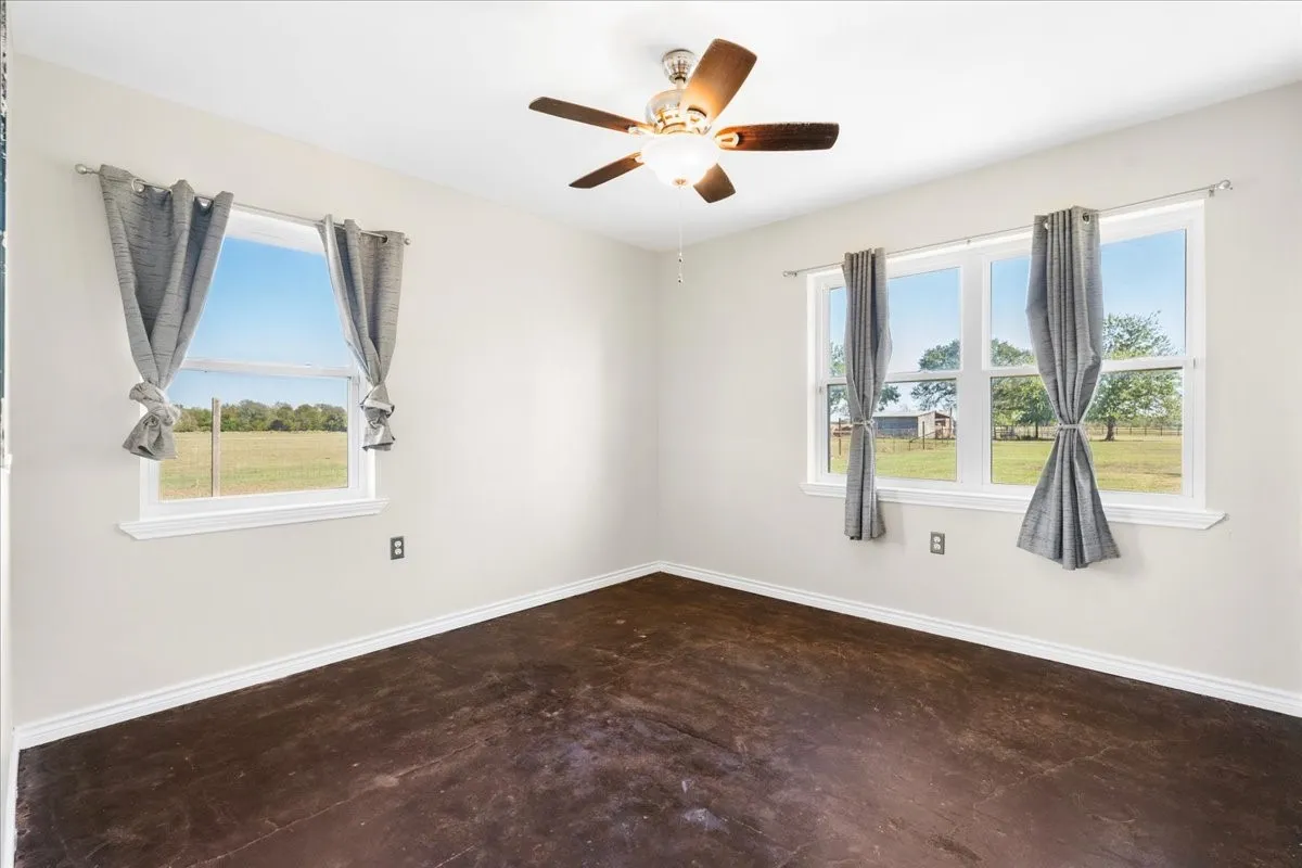 Wood-finish flooring with white trim, light-colored walls, and a ceiling fan with integrated lighting