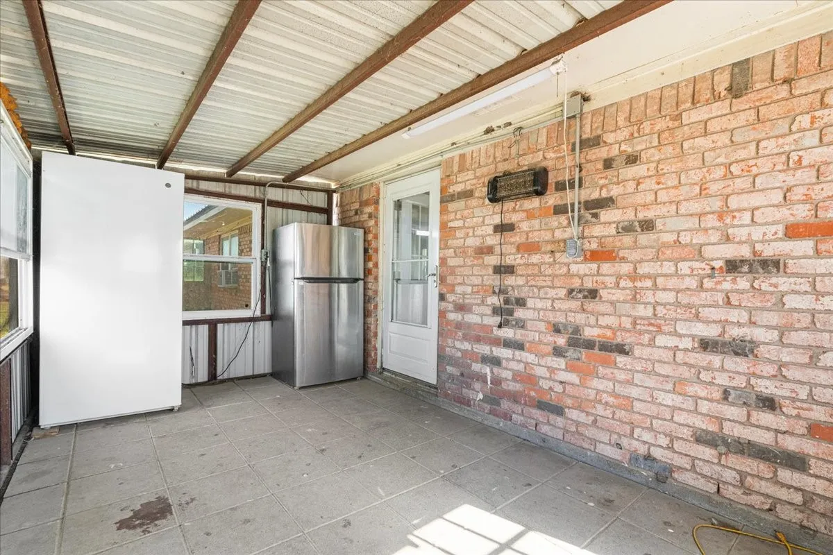 Screened-in porch featuring a brick exterior wall, tile flooring, and a corrugated metal roof