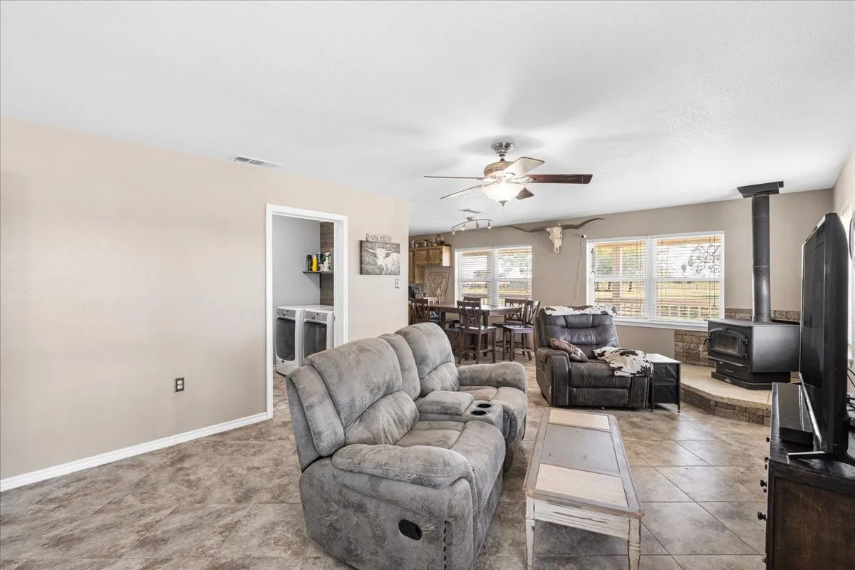 Spacious living area featuring tile flooring, a built-in wood-burning stove with a stone surround, and multiple windows