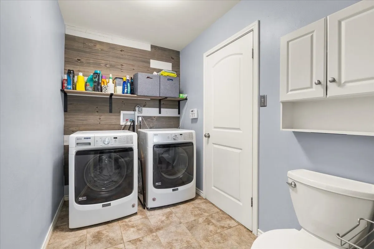 Laundry area featuring wood-finish wall paneling, open shelving, and neutral tile flooring