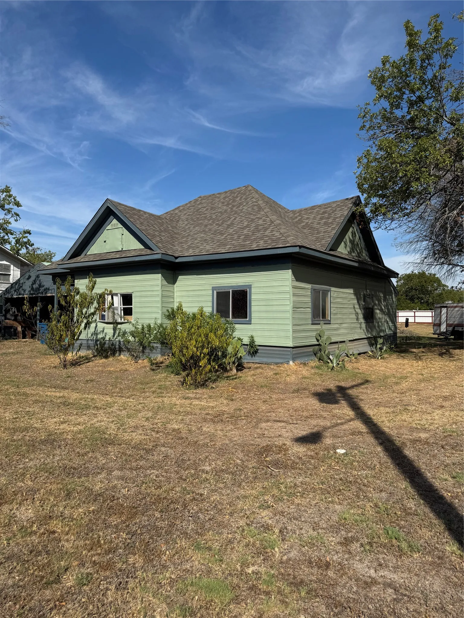 Gable roofline with asphalt shingles, light green horizontal siding, dark trim, and multiple windows