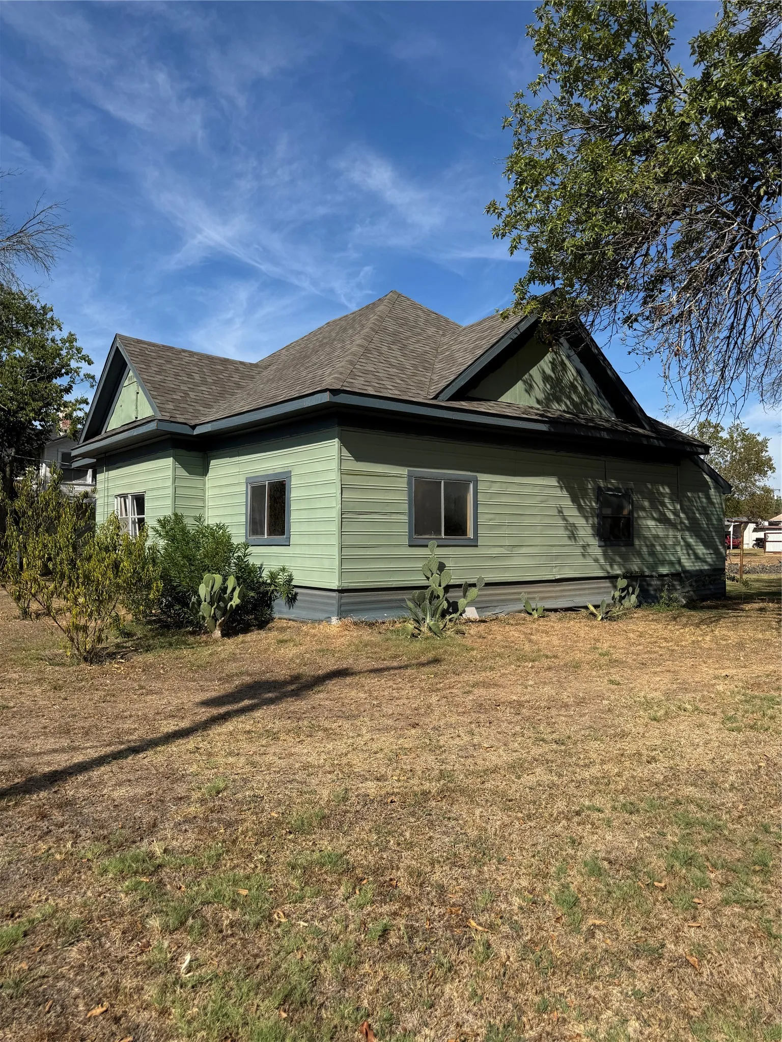 Green exterior siding with contrasting trim, multiple windows, and a shingle roof