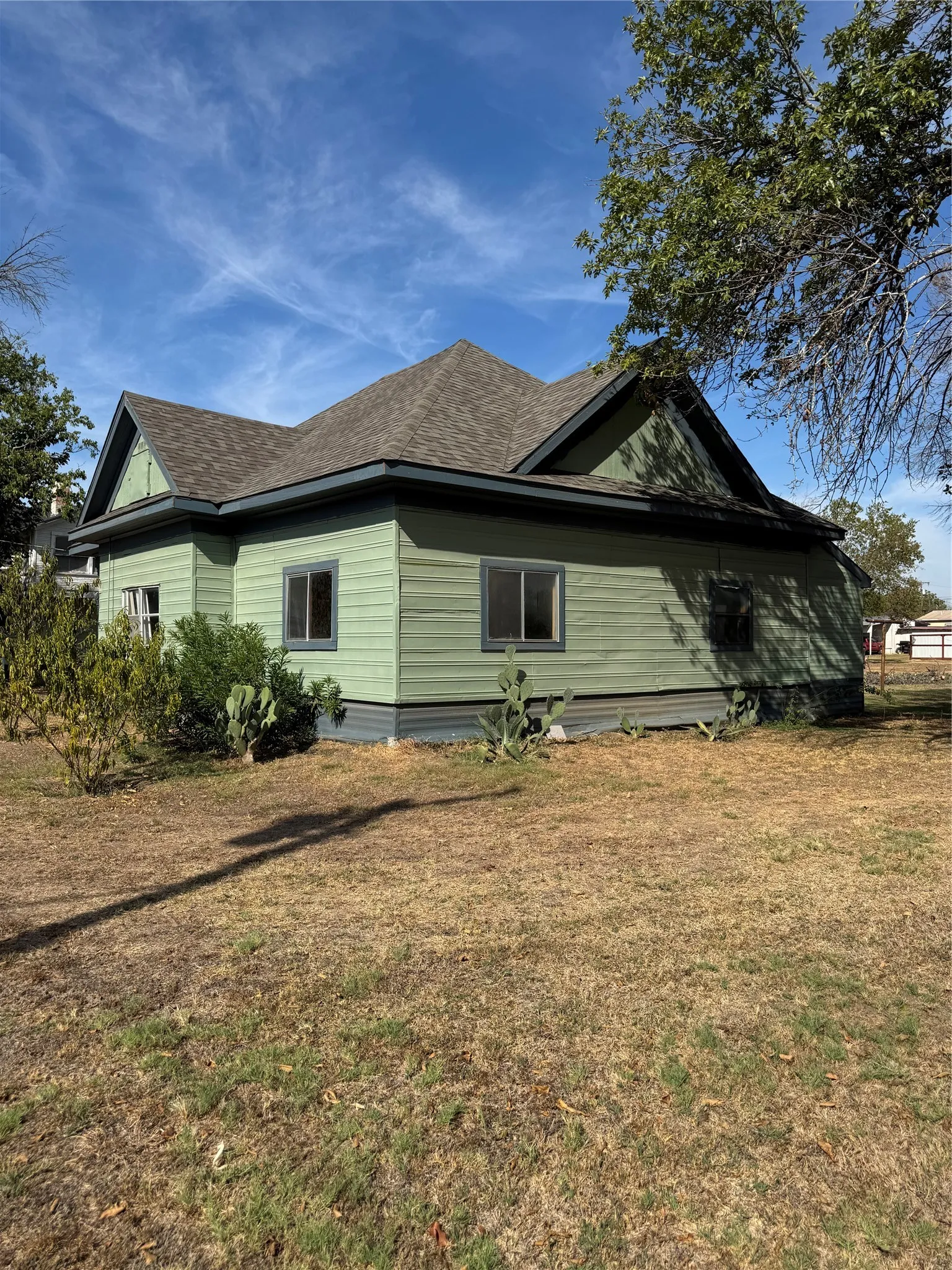 Pitched shingle roof with dark trim, green horizontal siding, and multiple windows