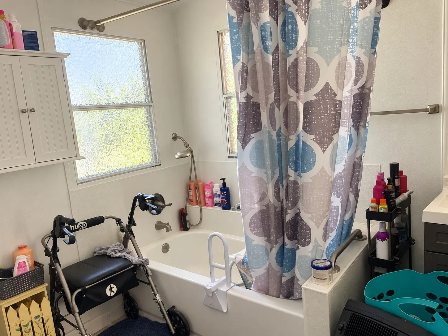 Bathtub with showerhead and grab bar, featuring two privacy windows and a wall-mounted storage cabinet