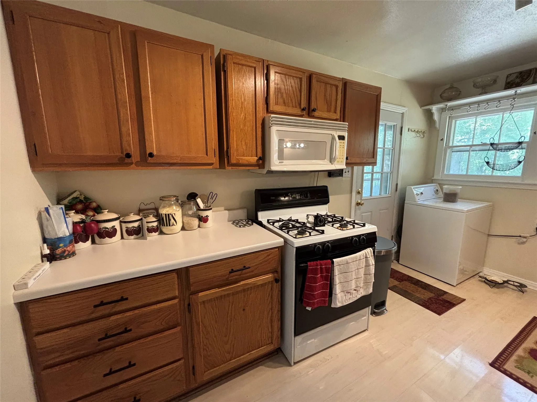 Wood-finish cabinetry with black hardware, white countertop, white gas range, and a built-in microwave