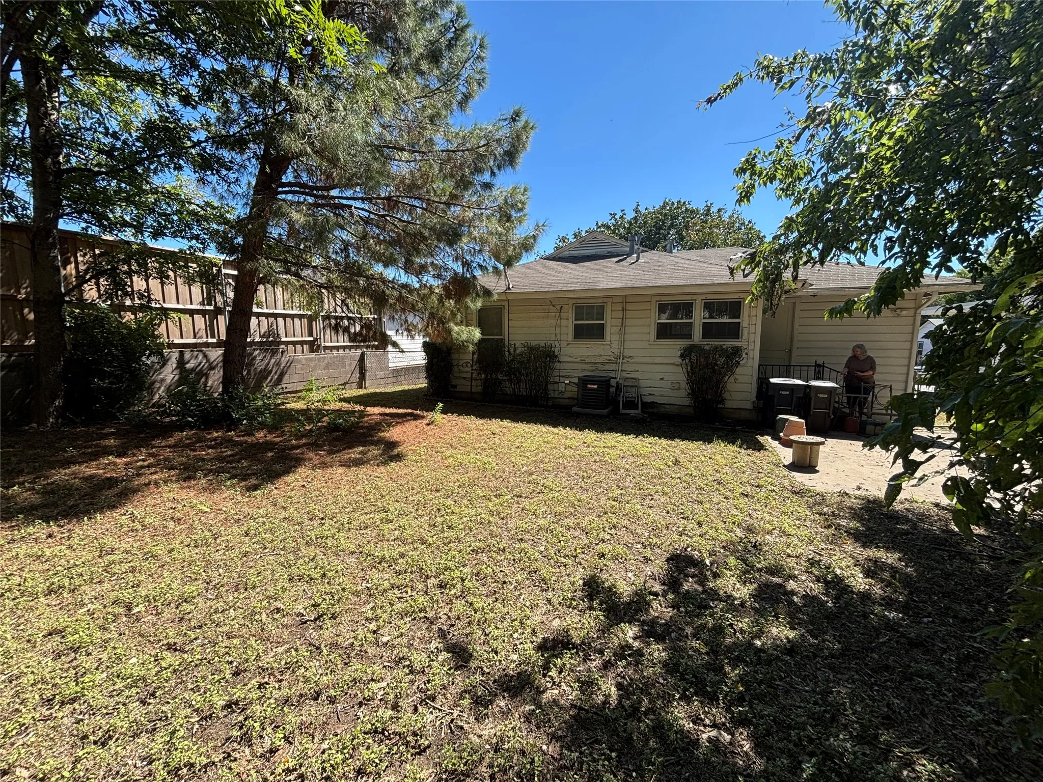 Expansive yard with mature trees, a privacy fence, and a concrete patio