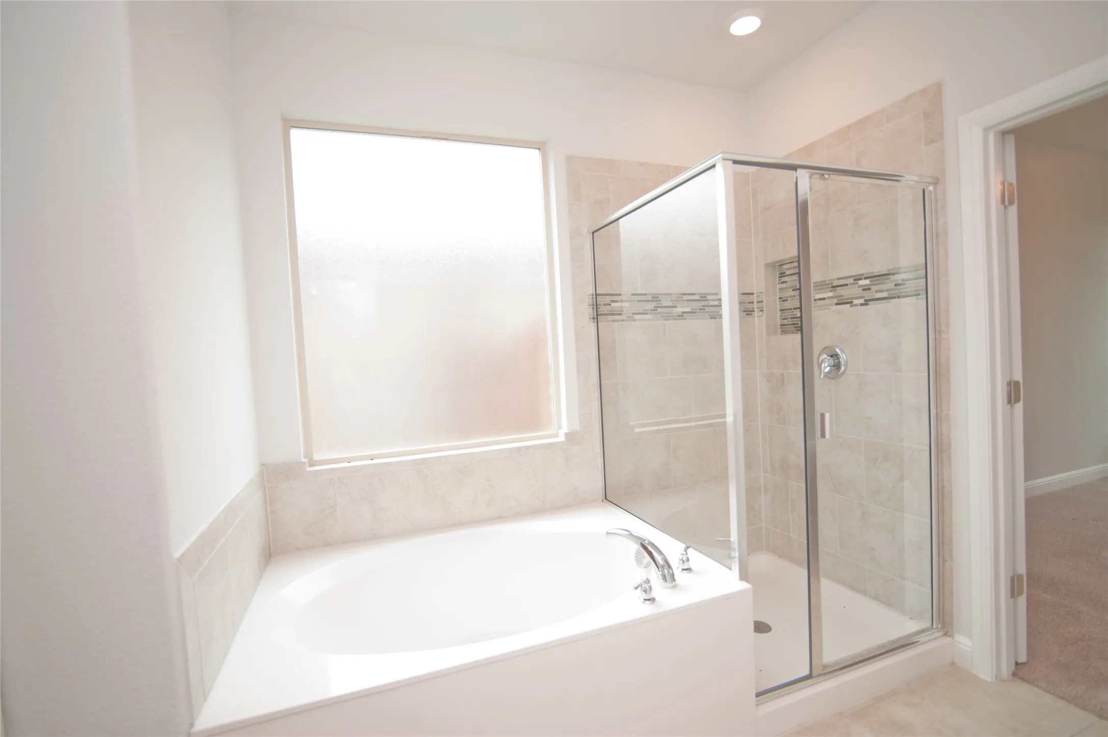 Alcove soaking tub with chrome fixtures, glass-enclosed shower with tiled walls and decorative accent band, and recessed lighting
