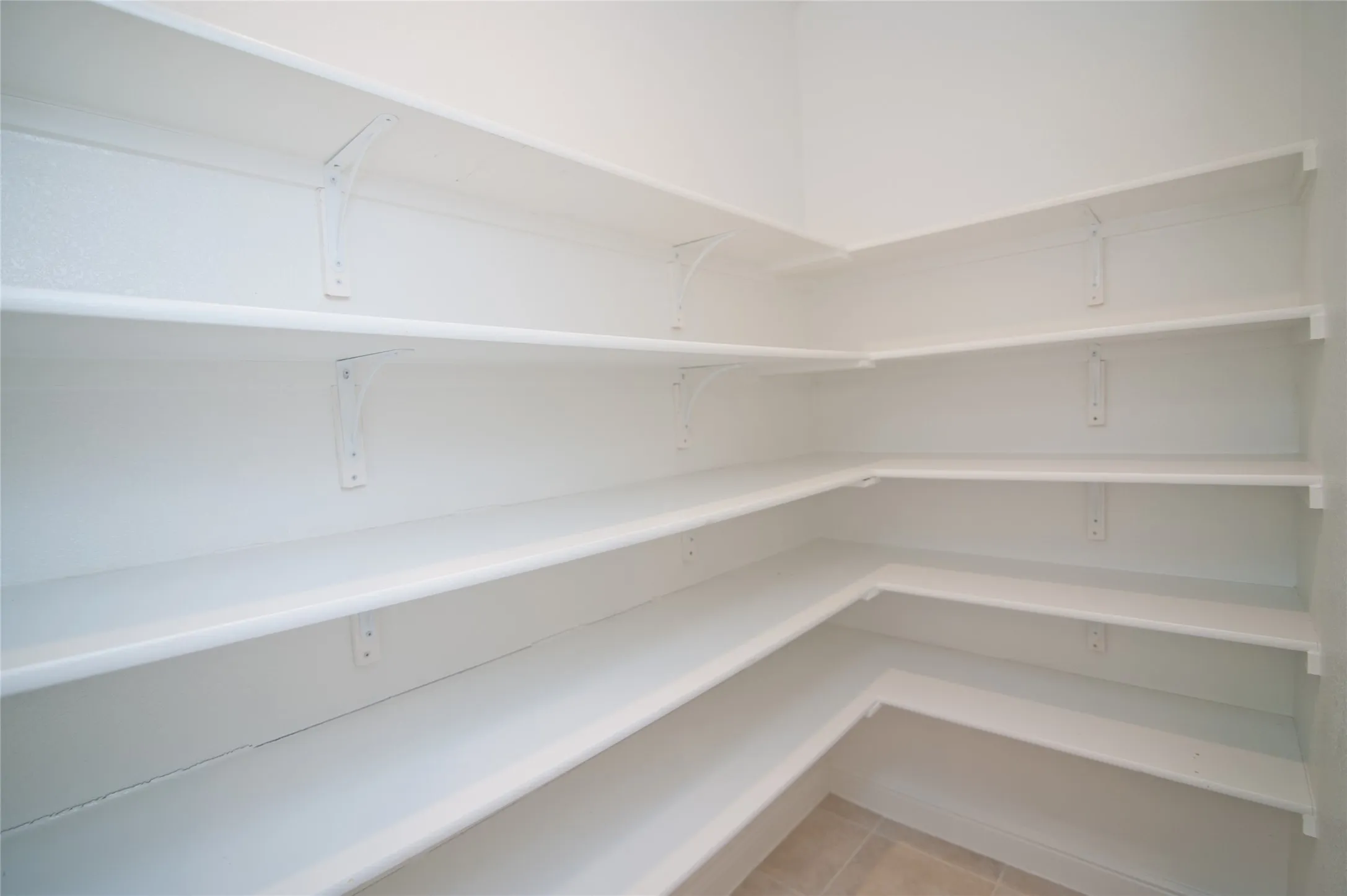 Extensive corner pantry with multiple white shelves and tile flooring