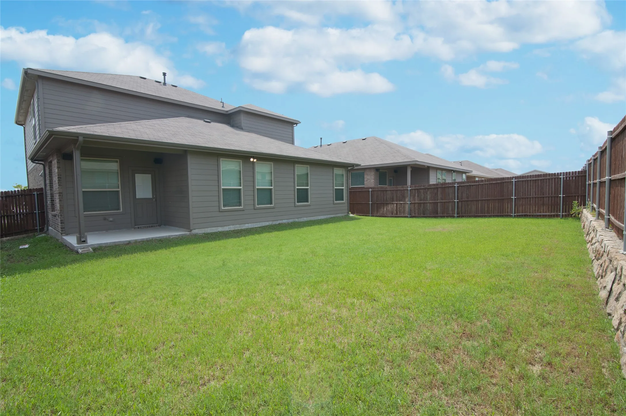 Expansive lawn with a wooden privacy fence, a covered patio, and multiple windows