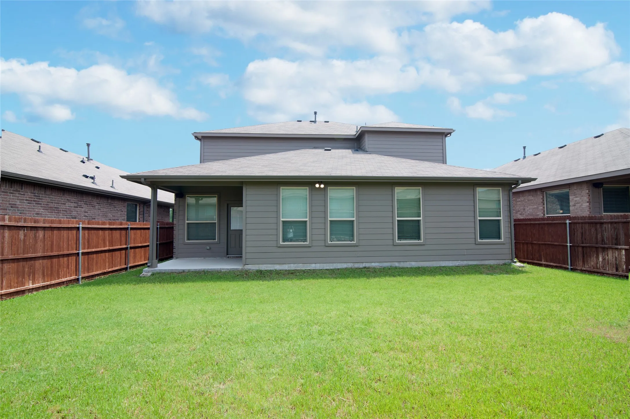 Expansive green lawn, privacy fencing, covered patio, and multi-pane windows