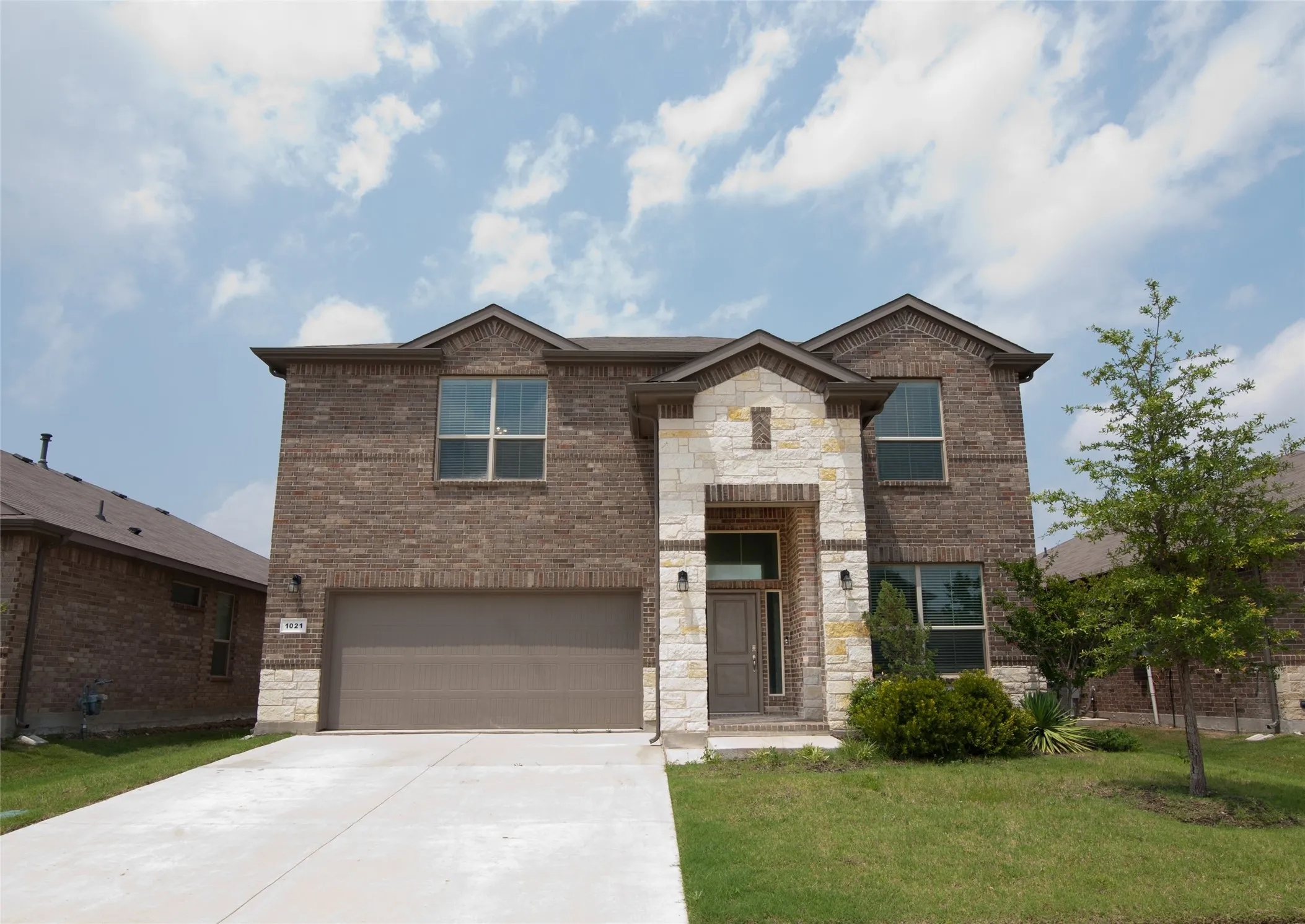 Two-story exterior with brick and stone accents, an attached garage, a concrete driveway, and a manicured lawn