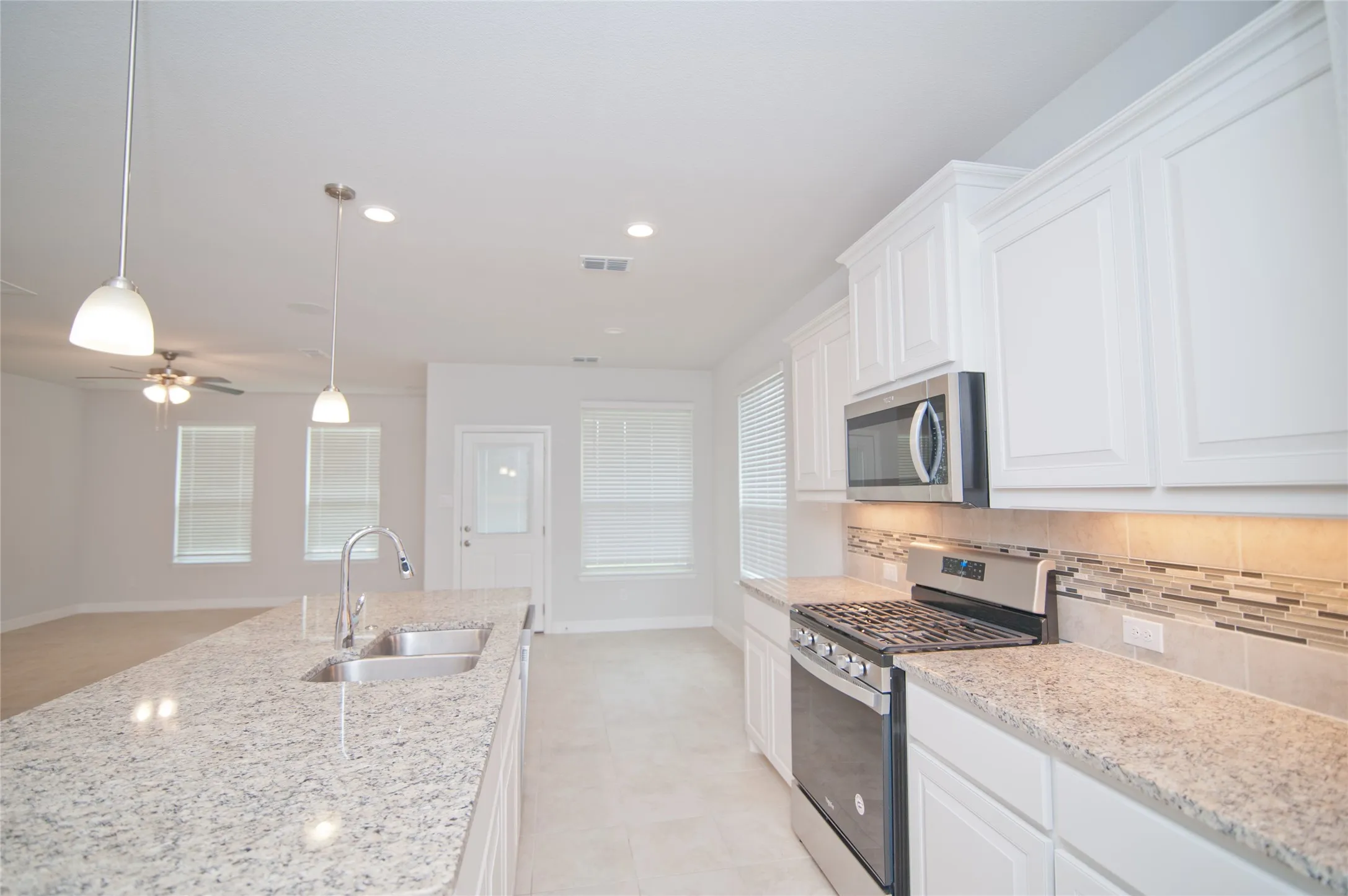 Kitchen featuring white cabinetry, light-toned countertops, stainless steel appliances, and a mosaic tile backsplash