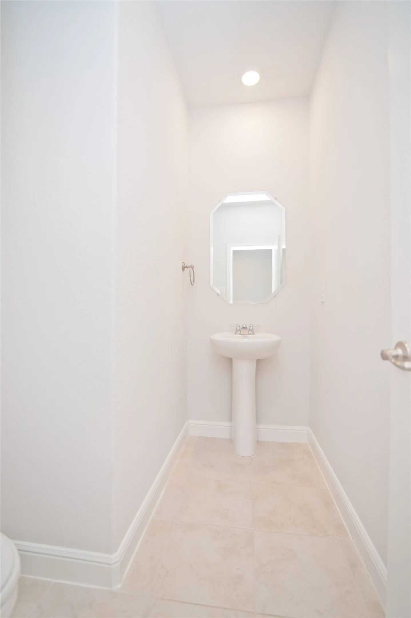 Recessed ceiling lighting illuminates a pedestal sink with a polished chrome faucet, set against tile flooring