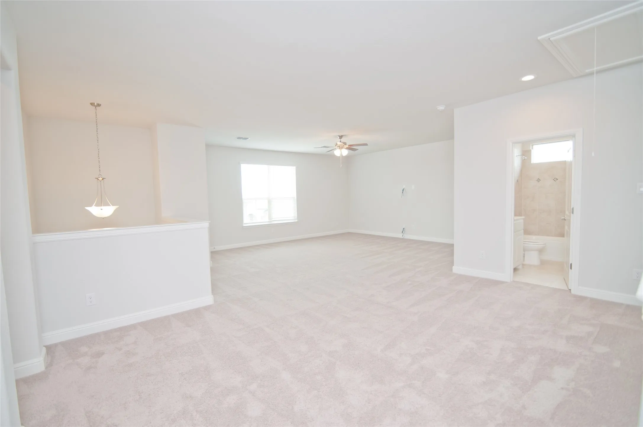 Expansive carpeted room featuring a ceiling fan, recessed lighting, and a pendant light fixture