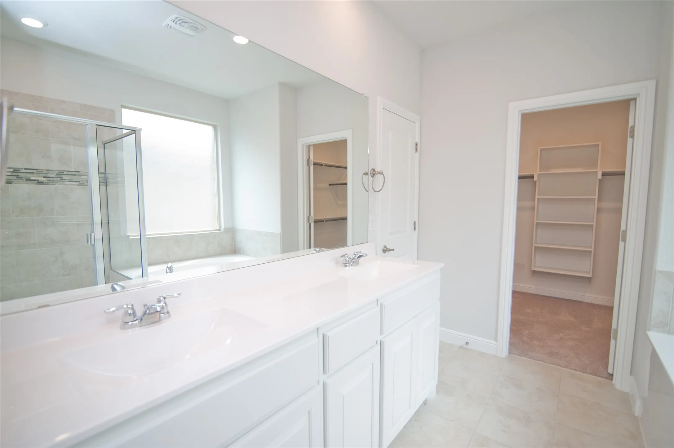 Dual vanity with white cabinetry, polished chrome fixtures, and a large wall mirror