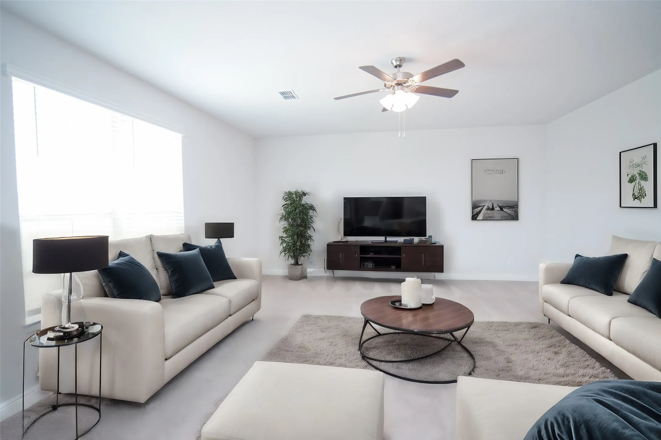 Spacious living area featuring light-toned flooring, white walls, and a ceiling fan with integrated lighting