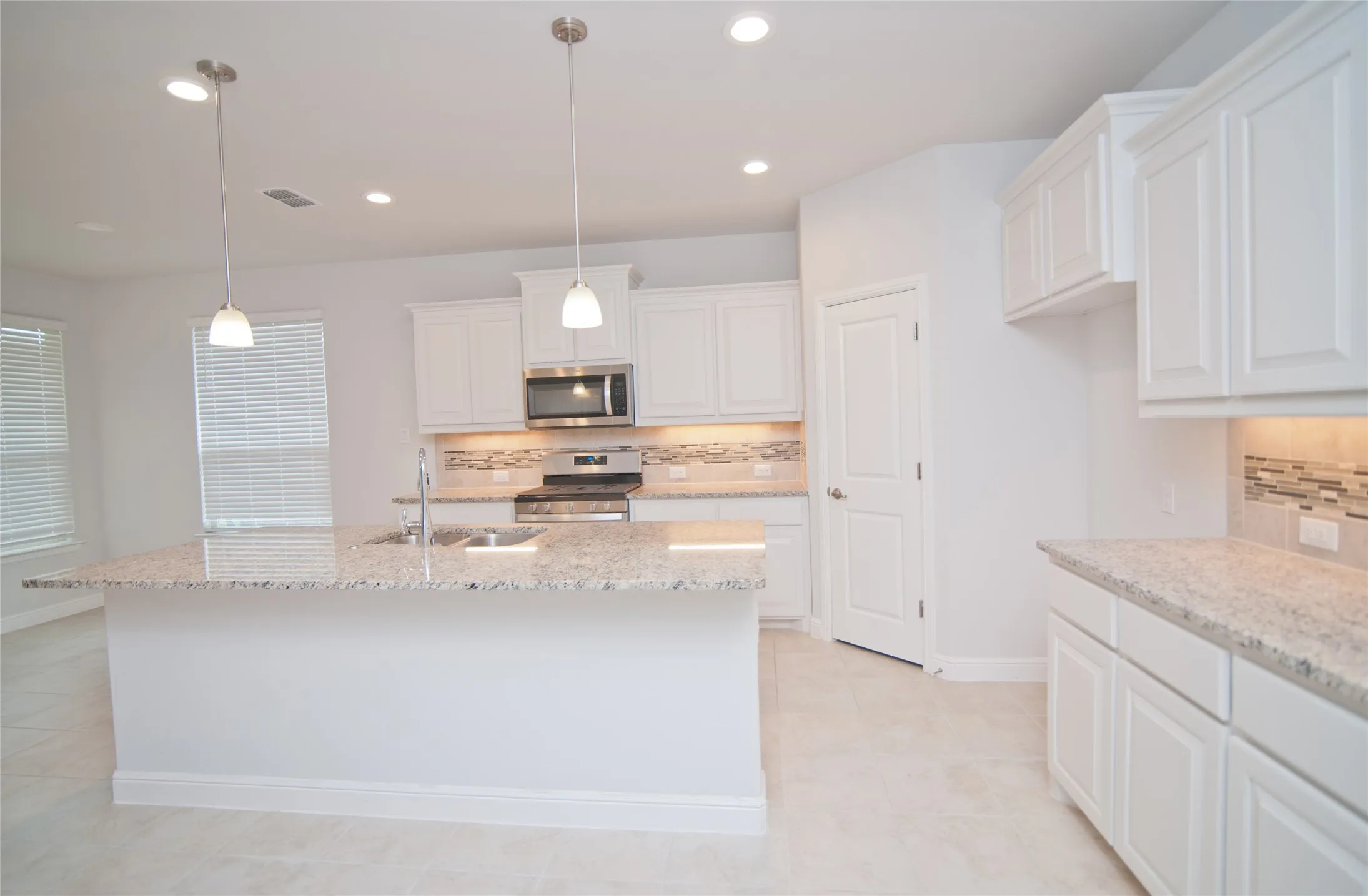Kitchen featuring a large island with sink, white shaker-style cabinetry, light-toned countertops, tile backsplash, and stainless steel appliances