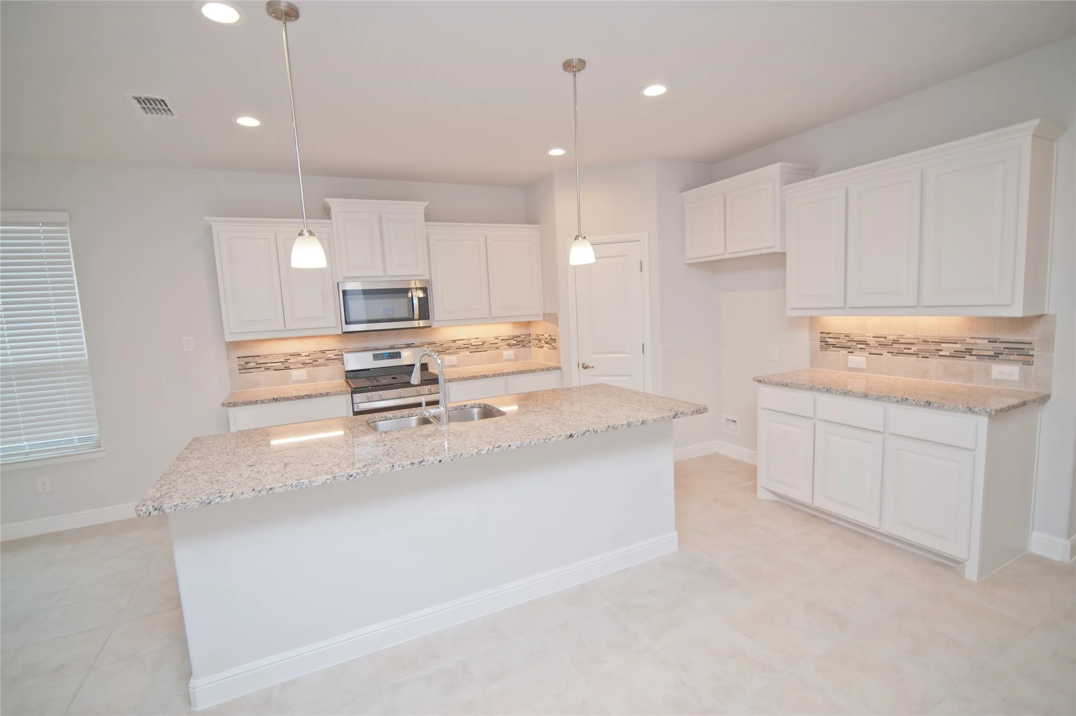 Kitchen featuring a central island with a double basin sink, stainless steel appliances, white cabinetry, granite countertops, and a tile backsplash