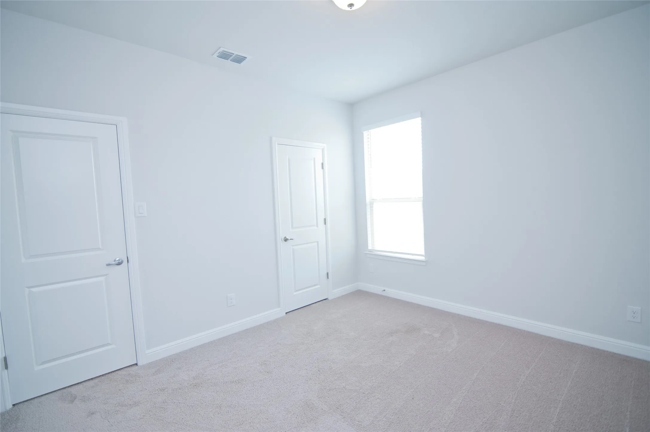 Neutral color palette, window with natural light, modern panel doors, flush mount ceiling light, carpeted flooring